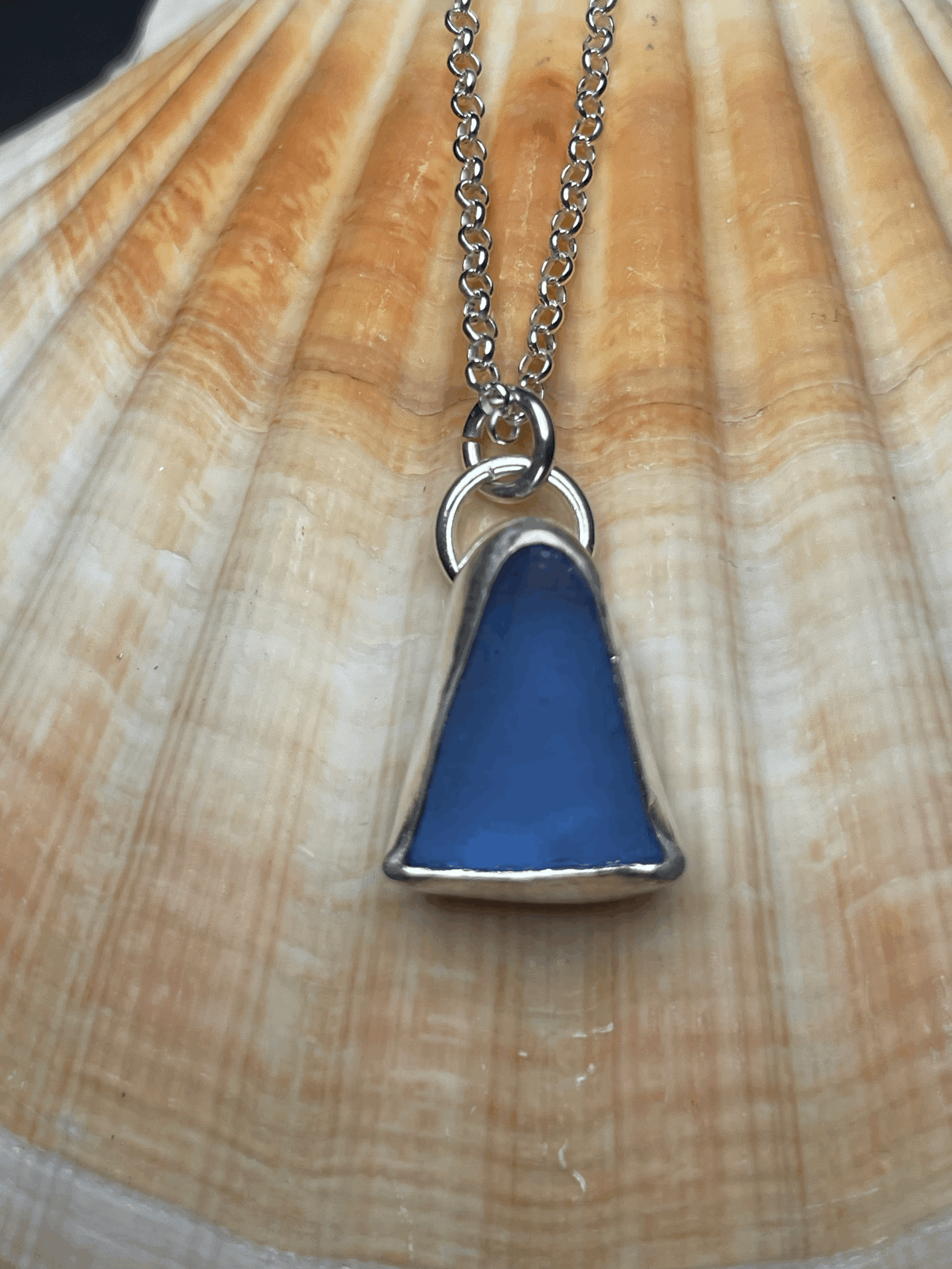A necklace with a large triangular blue pendant hanging from a silver chain, displayed on a textured wooden surface.