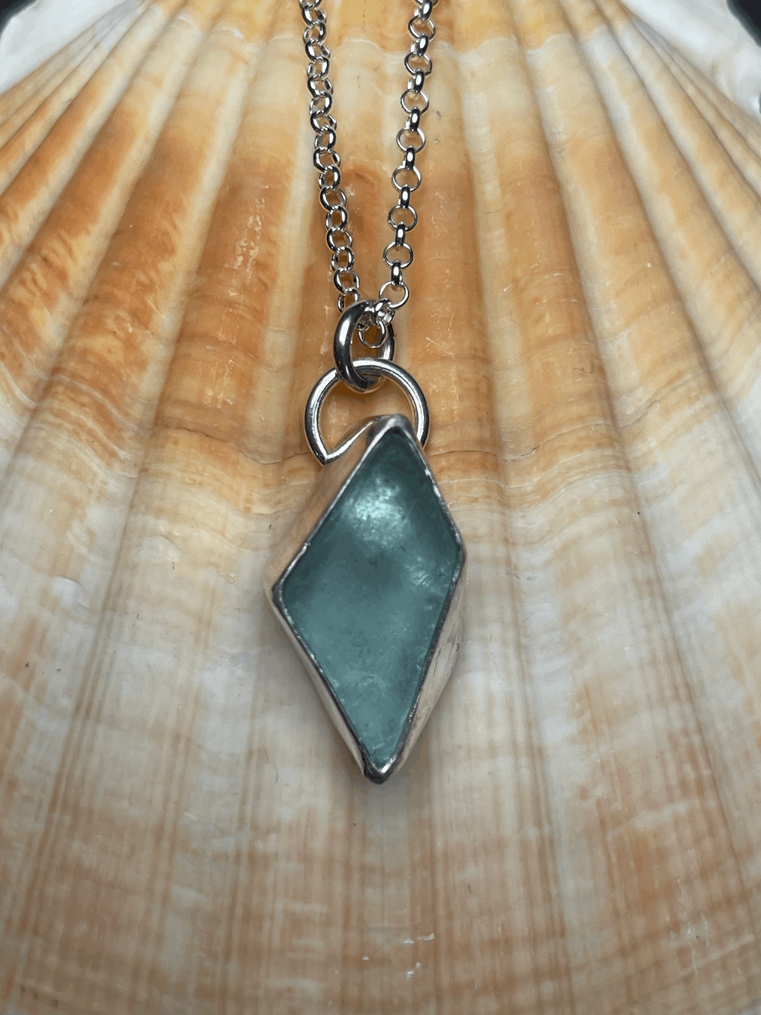 A silver necklace with a diamond-shaped turquoise pendant resting on a wooden surface.