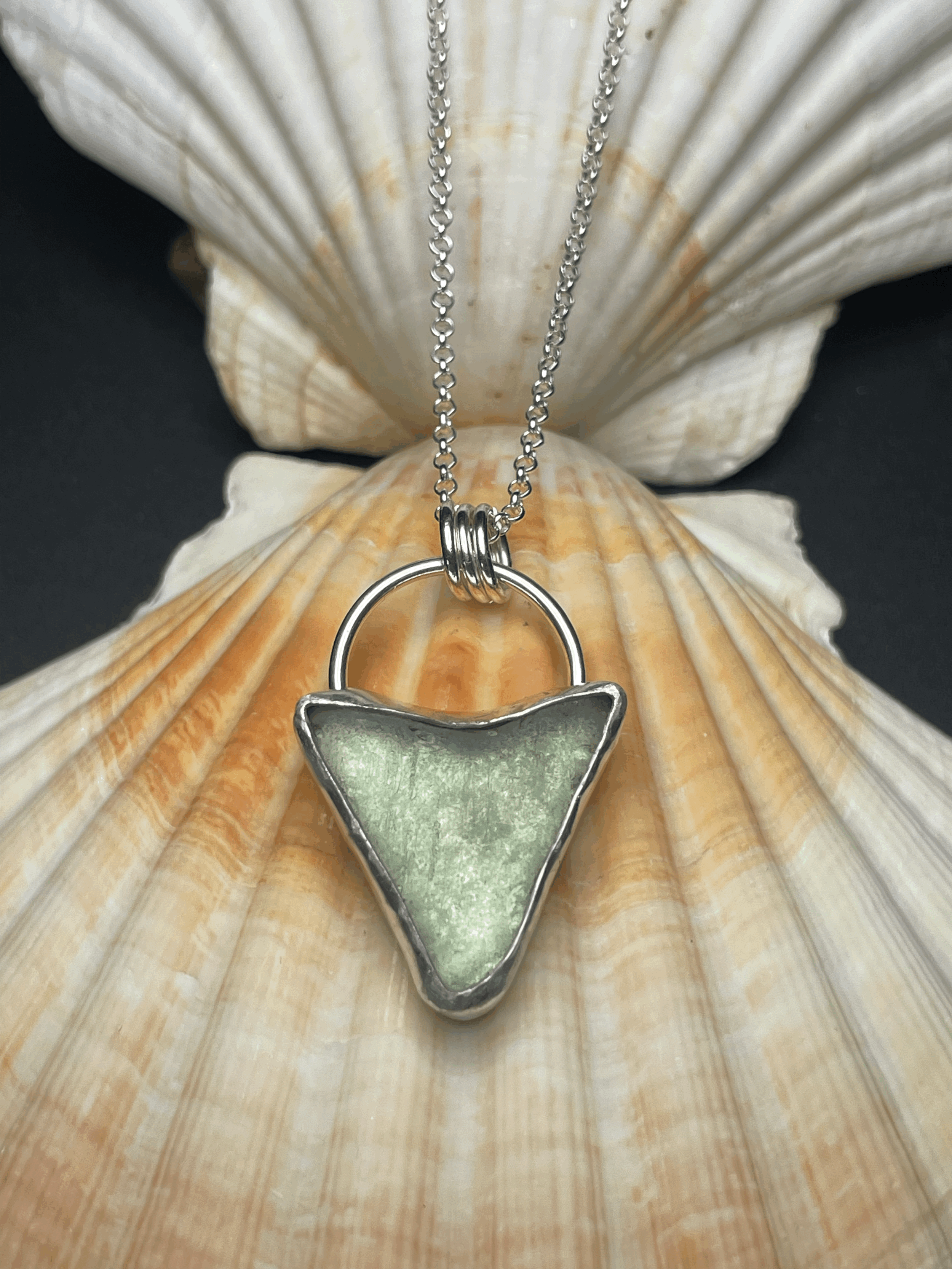Silver necklace with a green, triangular-shaped pendant resting on a scallop shell.