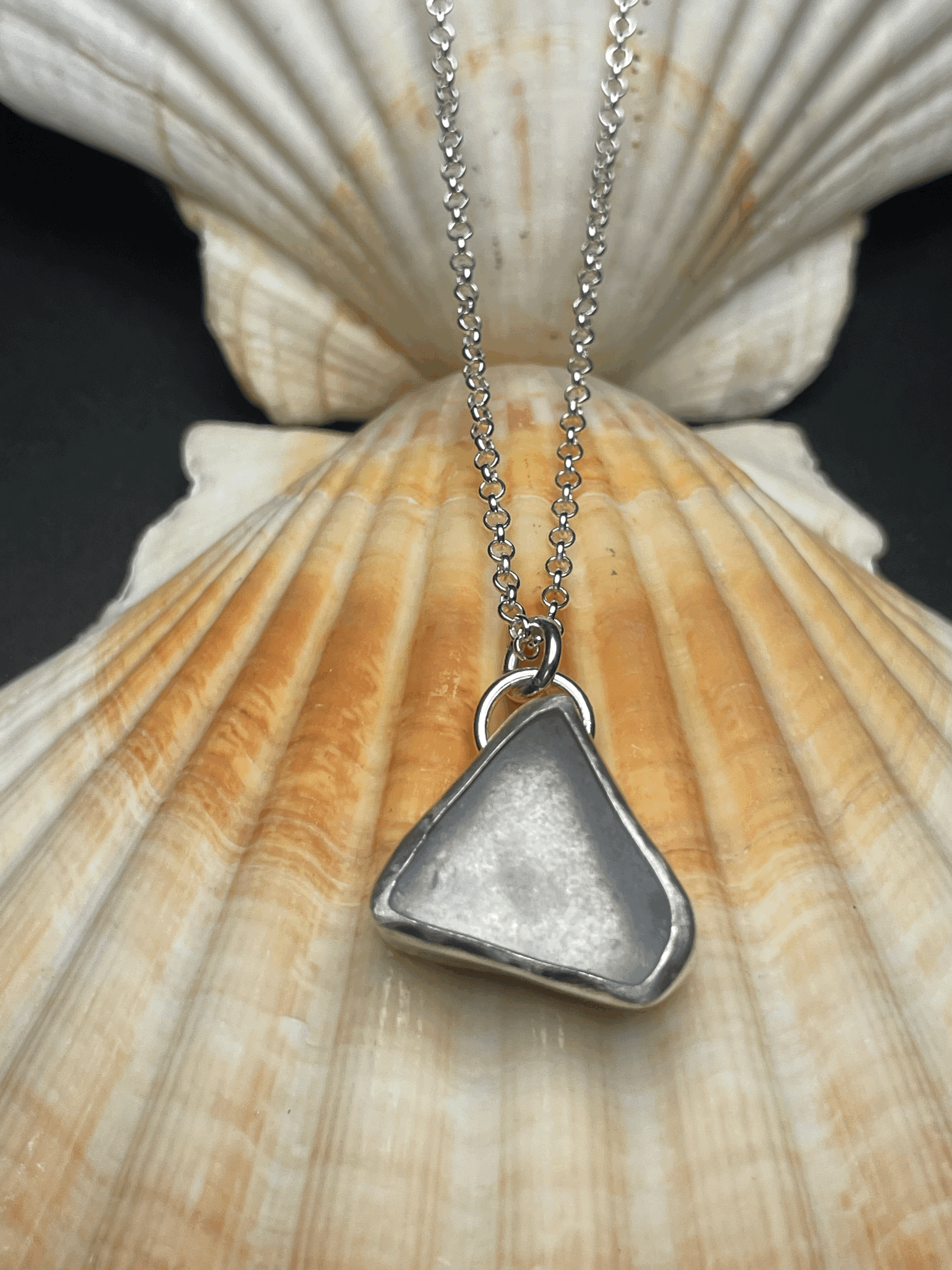 Silver triangular pendant necklace resting on a seashell.