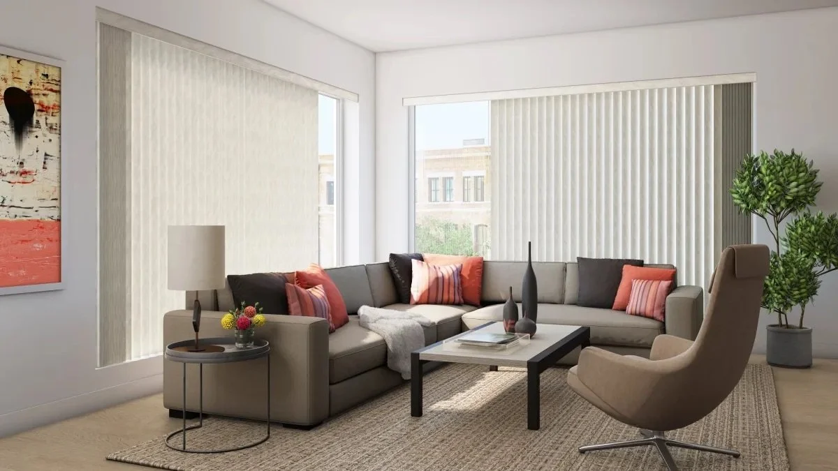 Modern living room with beige sectional sofa, recliner chair, coffee table, side table with lamp, colorful pillows, tall green potted plant, large windows with vertical blinds, and wall art.