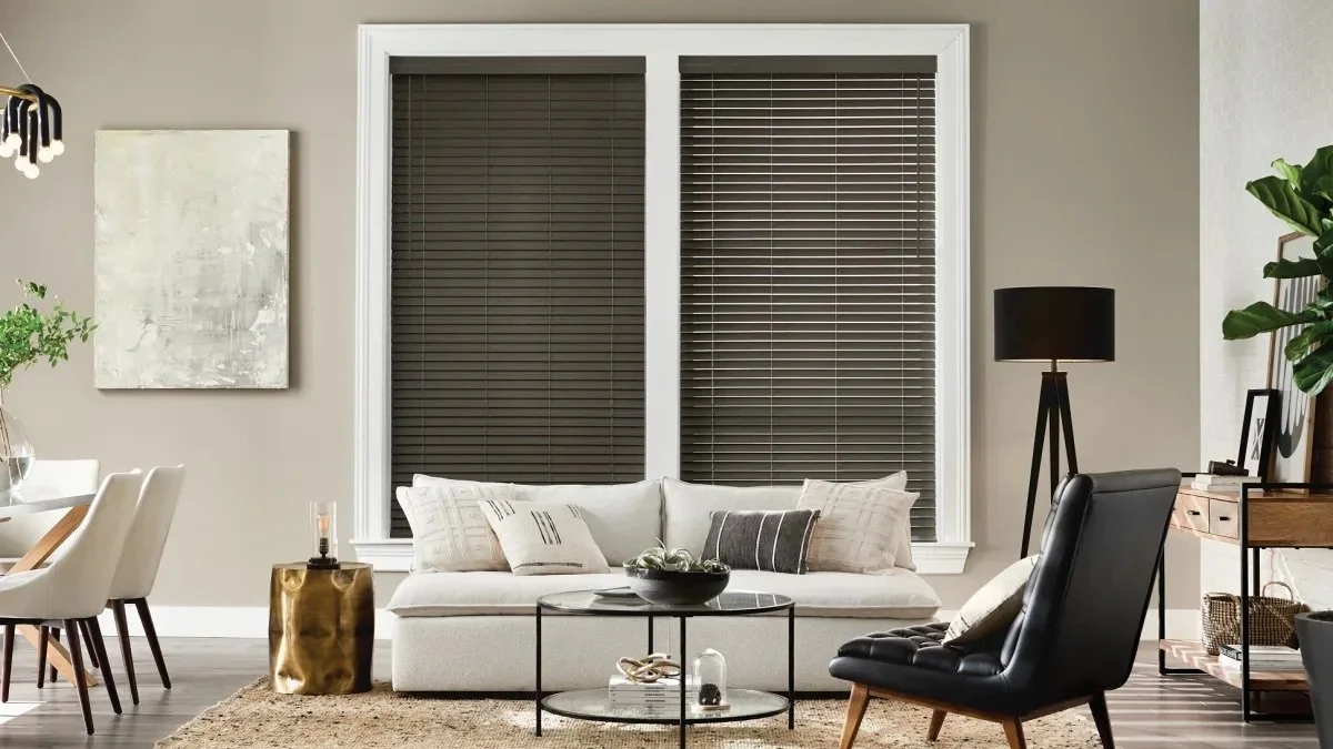 Modern living room with a white couch, black armchair, round coffee table, large window with dark blinds, and various decor items.