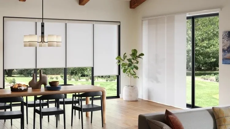 Modern dining area with a wooden table, black chairs, white cabinets, large windows, and a potted plant.
