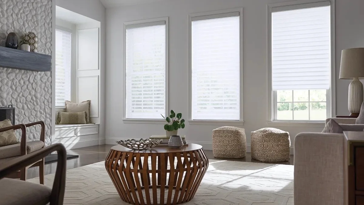 Bright living room with large windows, white walls, a round wooden coffee table, and beige furniture.