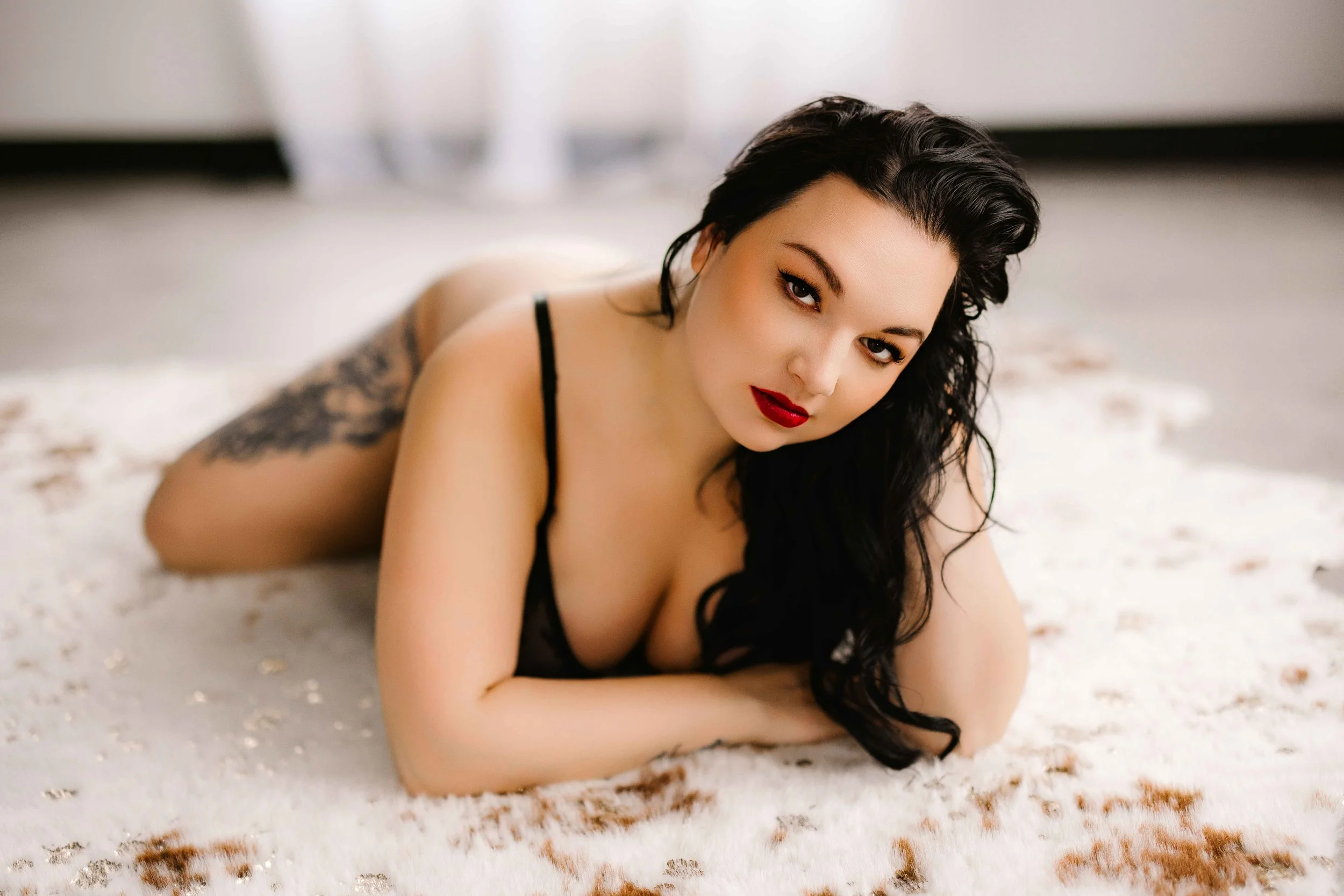Boudoir photo of Miss M in black lingerie lying on a plush rug, showcasing confidence and sultry expression