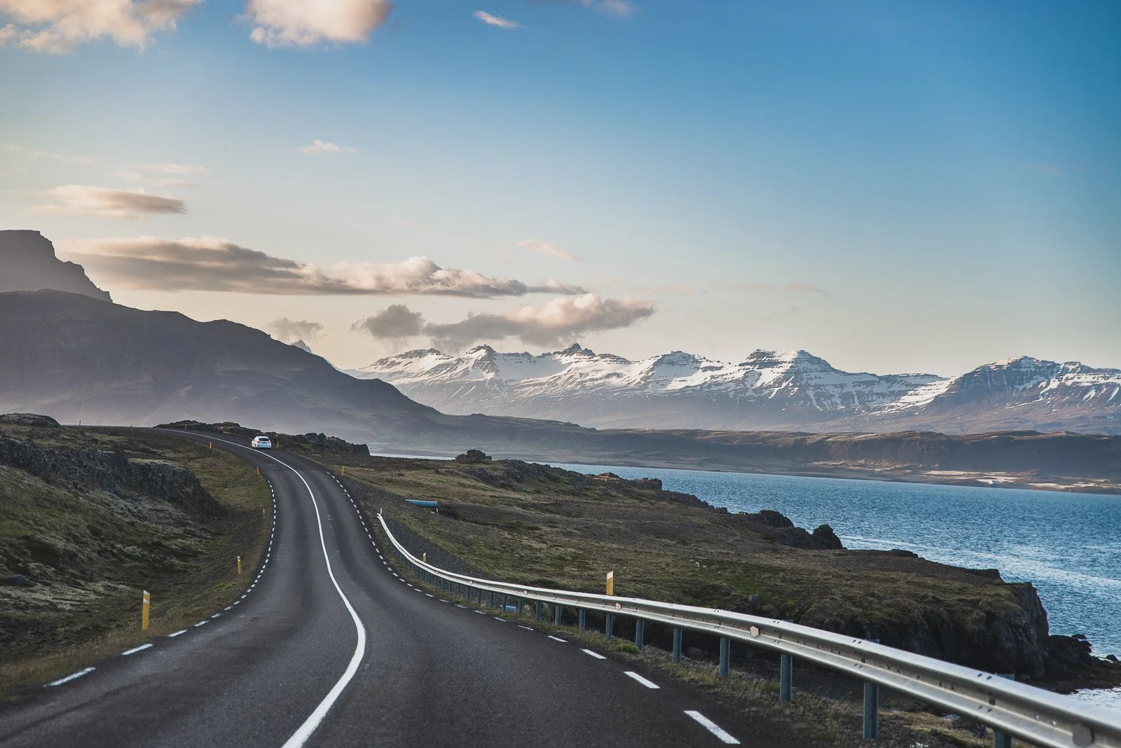 Winding coastal road beside the ocean with snow-covered mountains in Iceland