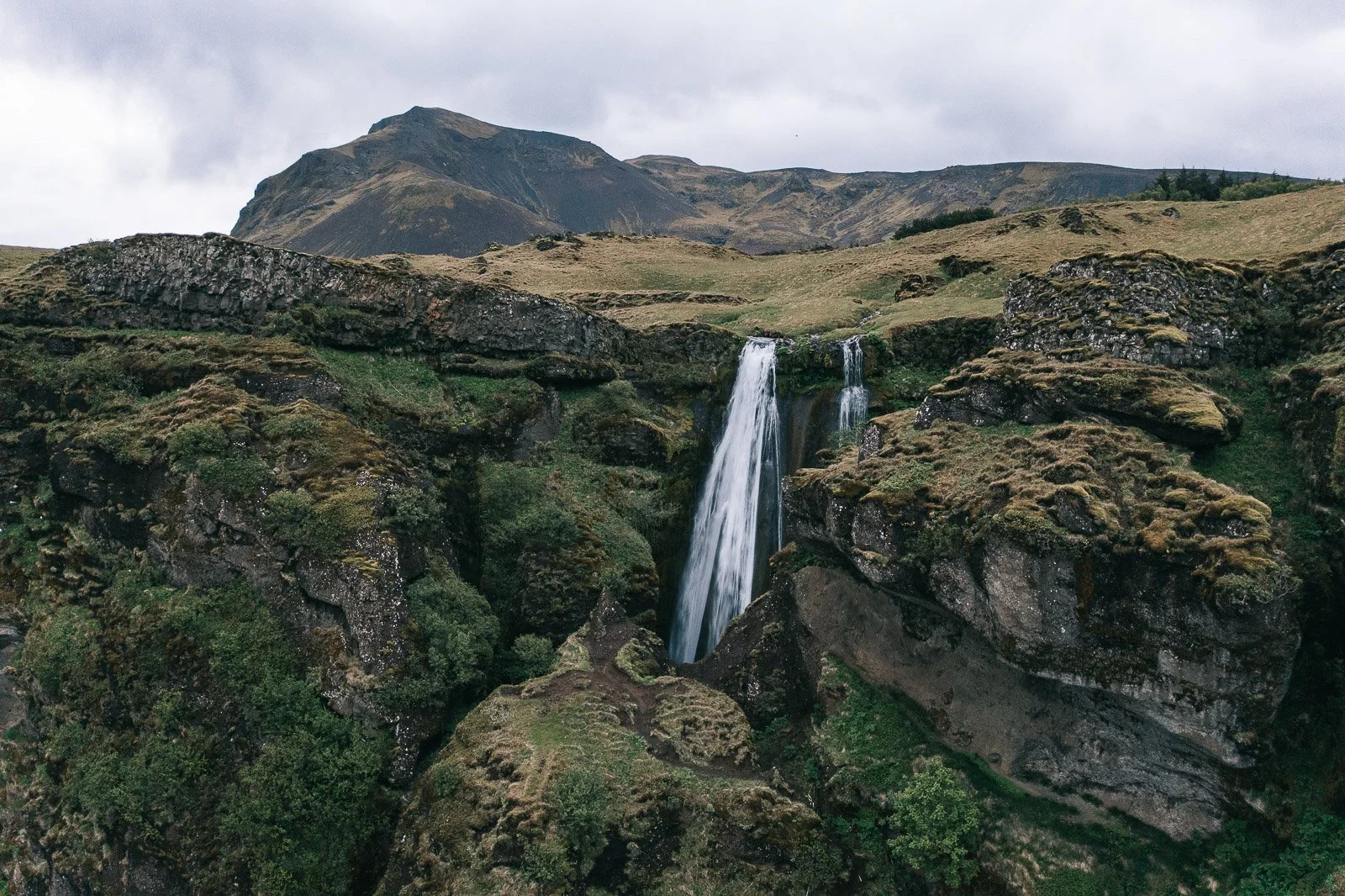 Waterfall dropping through a moss-covered canyon beneath mountains in Iceland