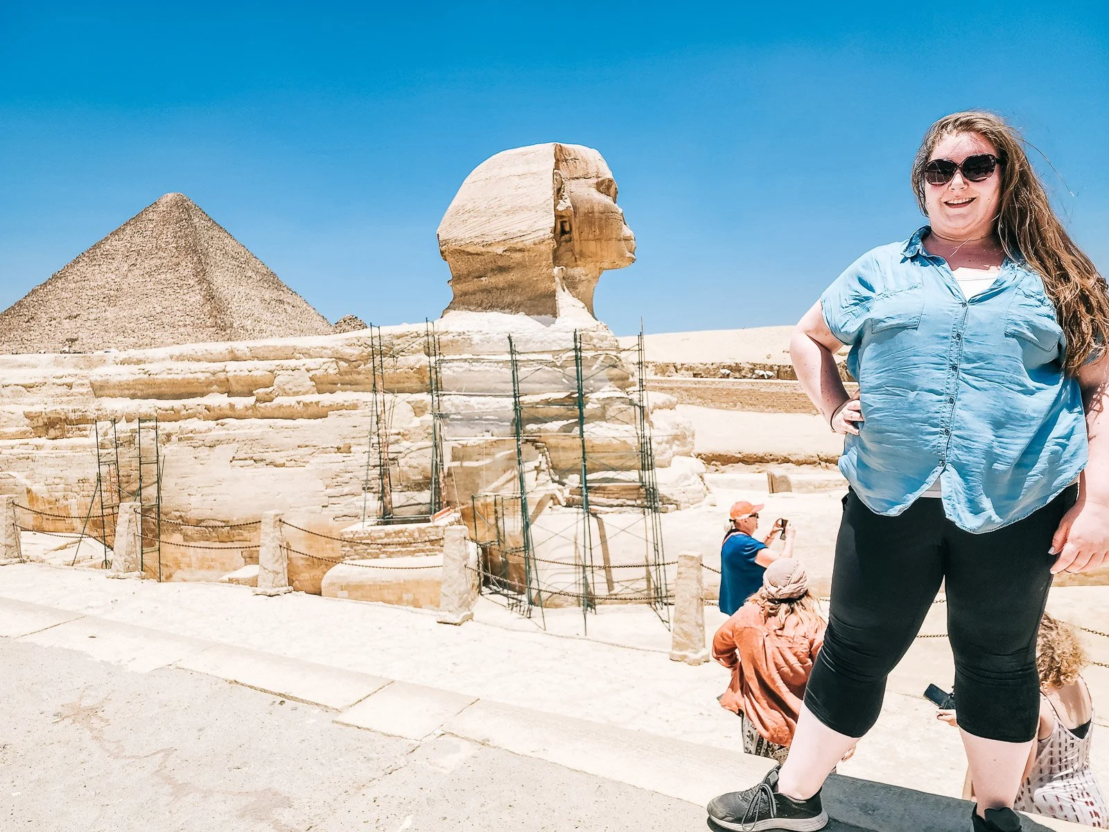 Traveler standing near the Great Sphinx with a pyramid in the background in Giza, Egypt
