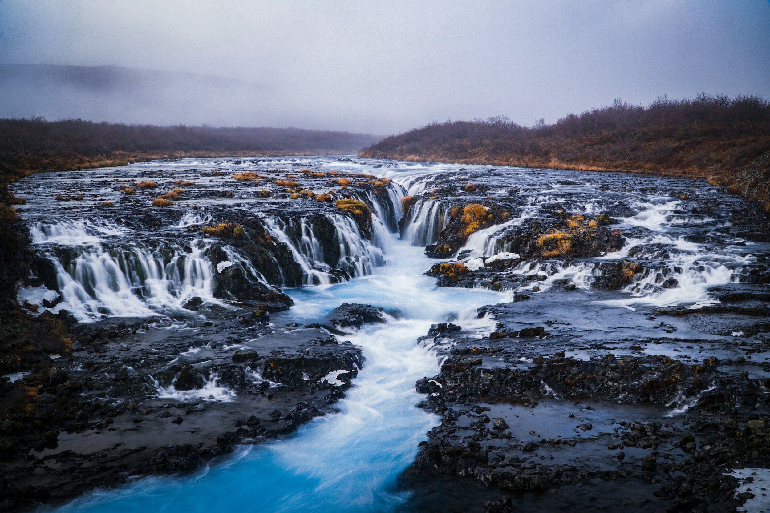 Brúarfoss waterfall flowing over dark volcanic rock into bright blue water in Iceland