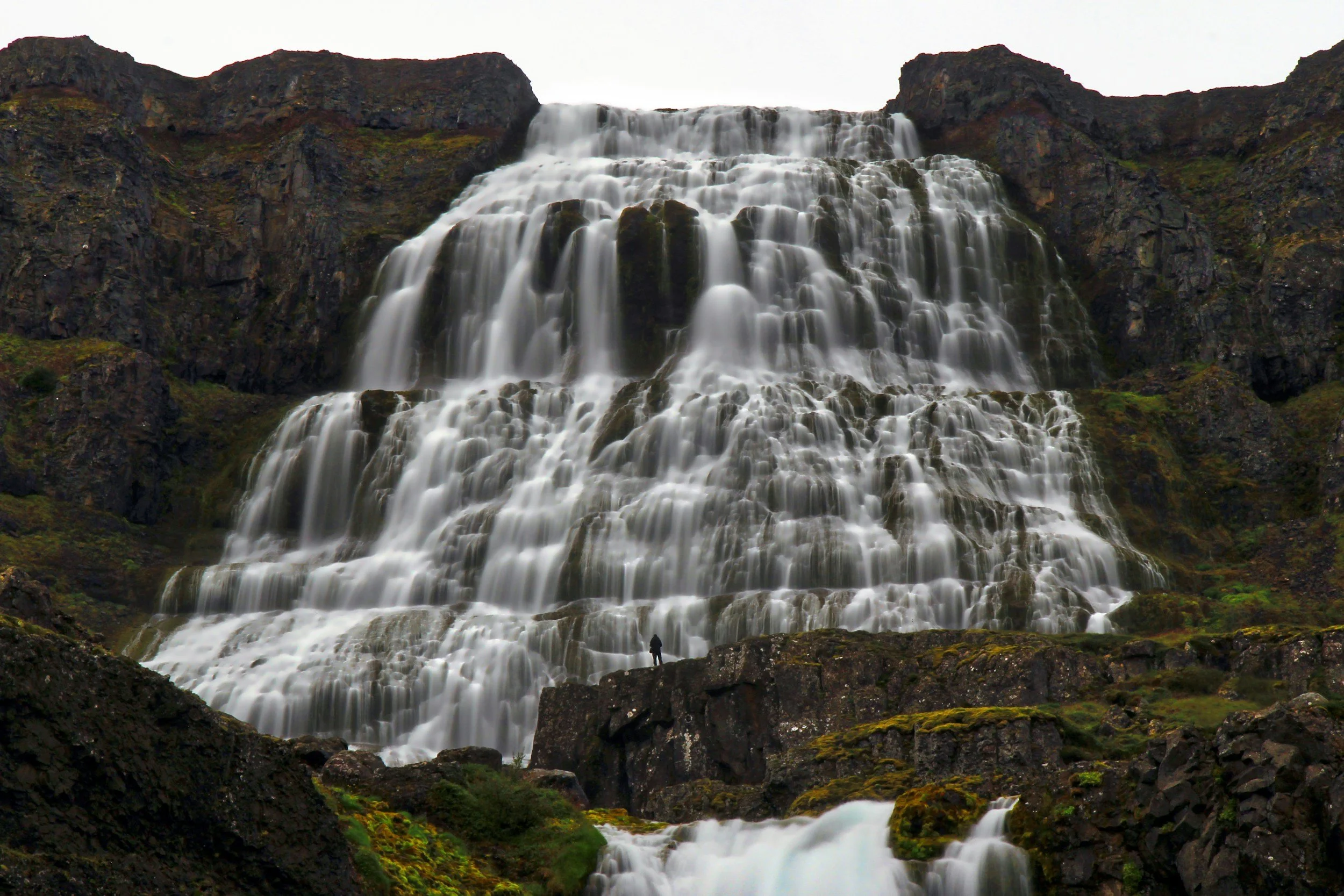 Dynjandi waterfall cascading in wide tiers down a mountainside in Iceland with a person below for scale