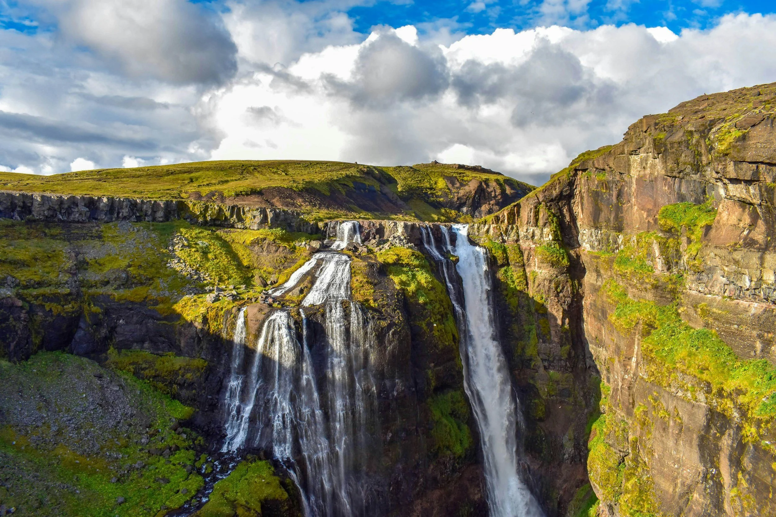 Glymur waterfall cascading down a green rocky canyon beneath dramatic clouds in Iceland