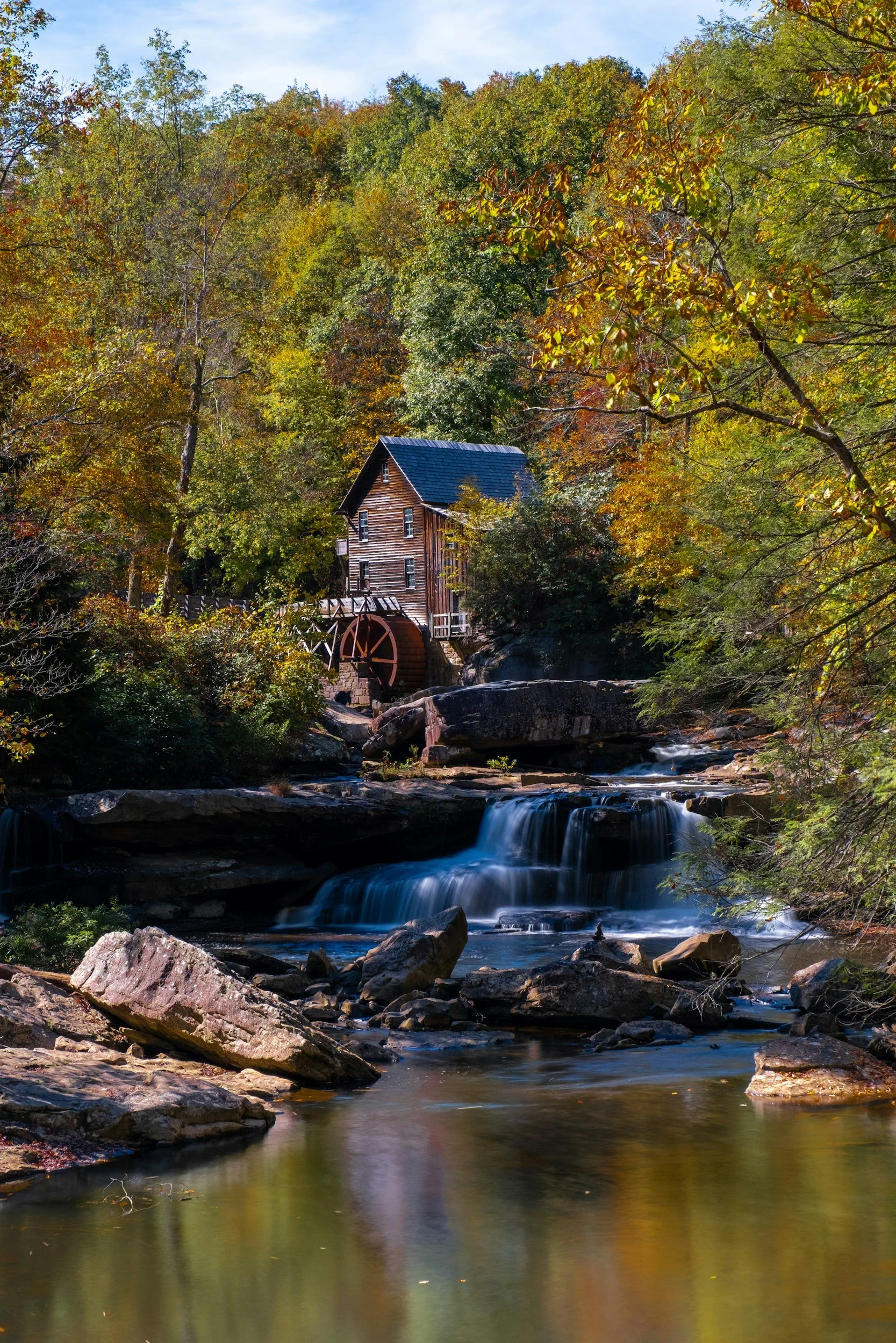 Image of a house with a waterfall in front leading into a pond surrounded by green trees