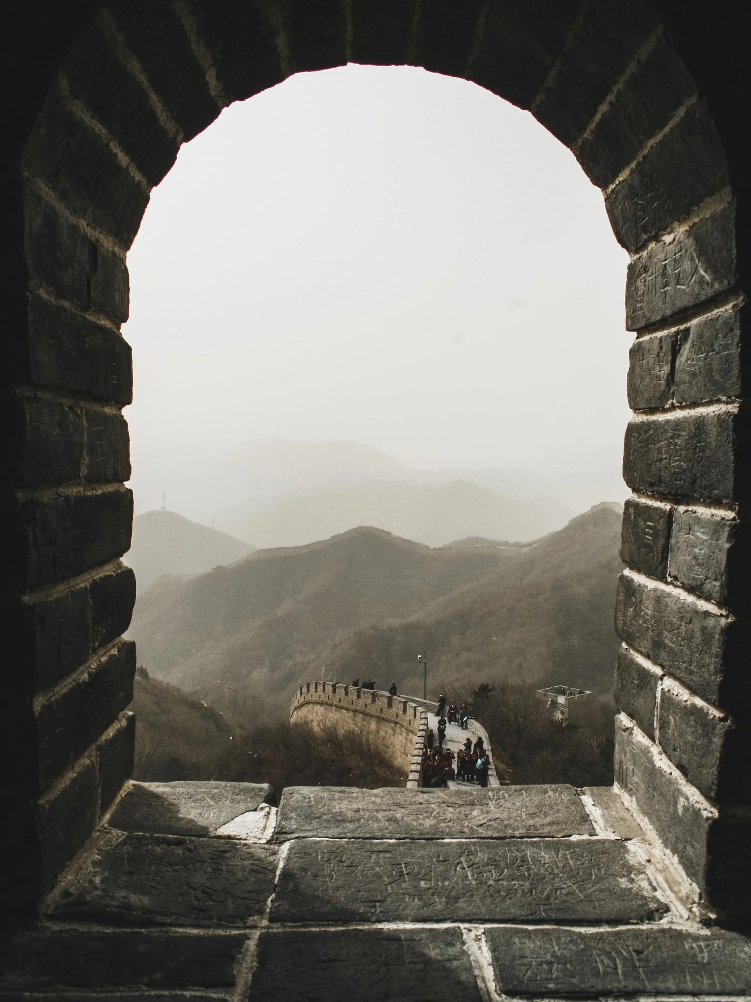 Great Wall of China viewed through a stone watchtower arch with mountains in the distance