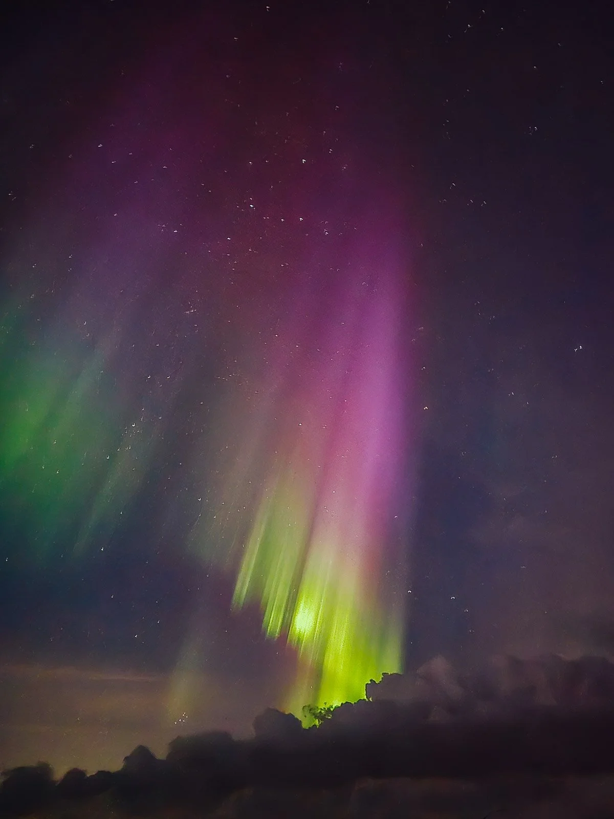 Green and purple northern lights glowing across a star-filled night sky above dark clouds.