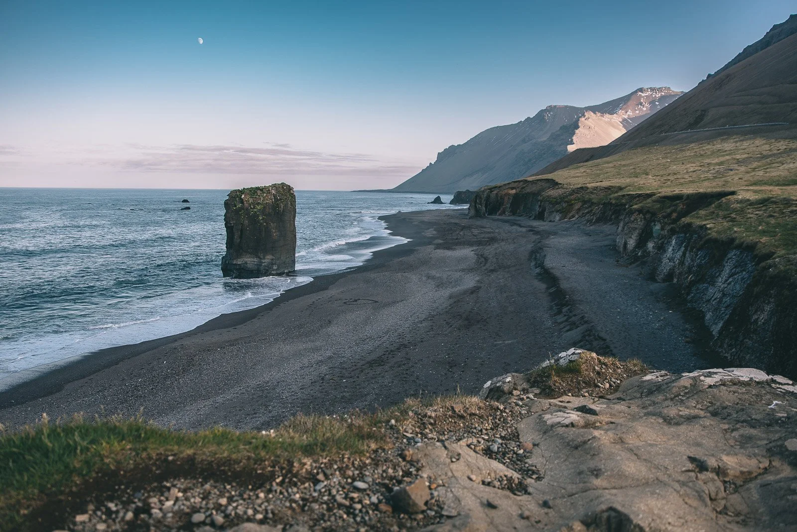Black sand beach with a large sea stack along Iceland's mountainous coastline