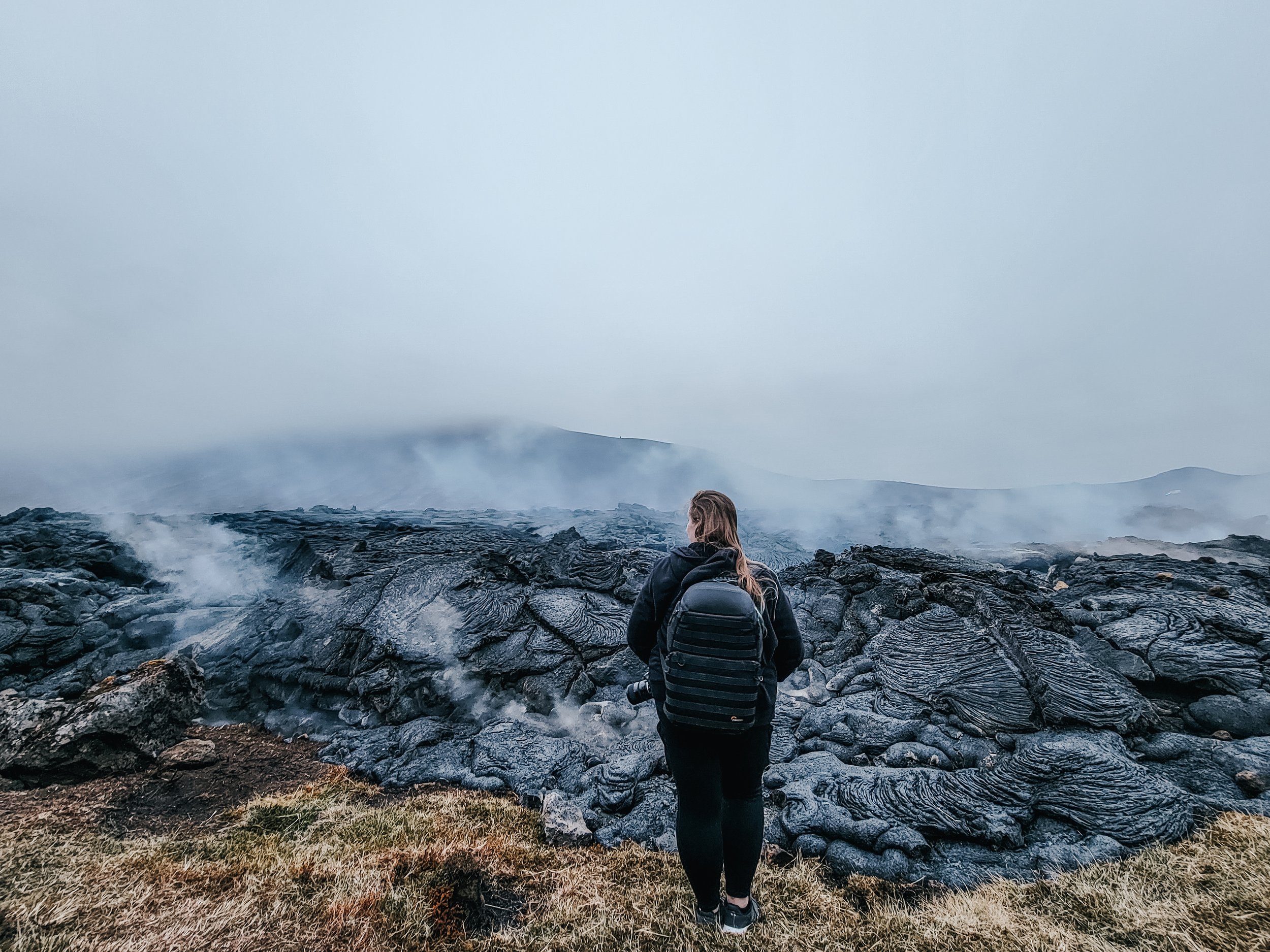 Traveler wearing a camera backpack beside a steaming lava field in Iceland