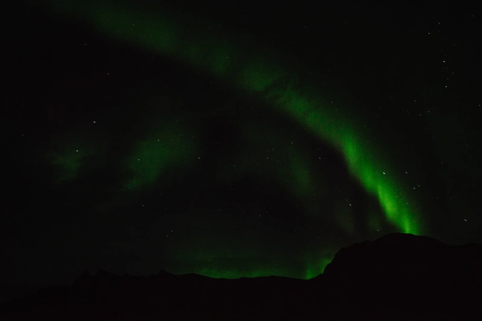 Green Aurora Borealis arching across the night sky above a mountain silhouette in Iceland