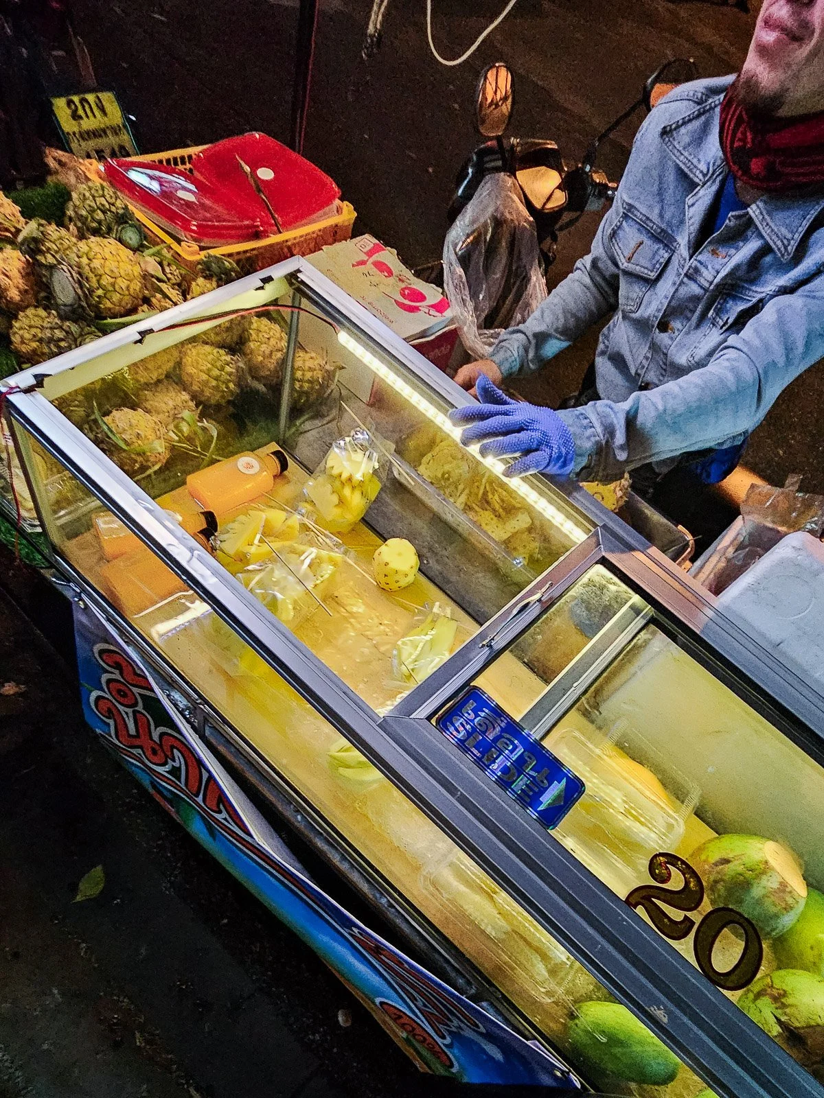Street vendor preparing cut fruit at a night market in Thailand.