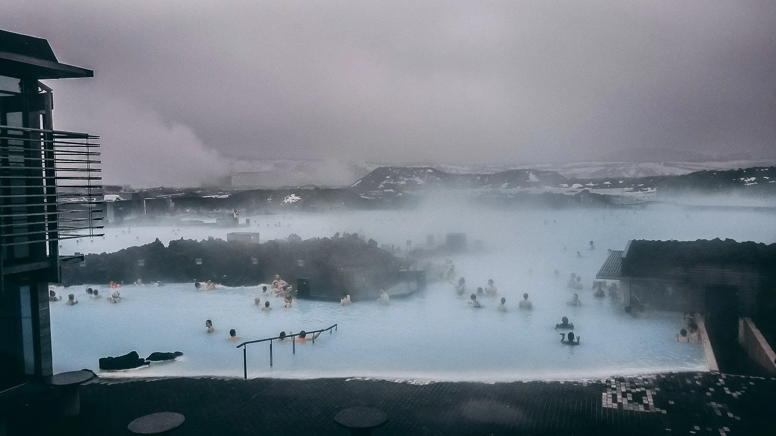 Steaming Blue Lagoon geothermal spa in Iceland with people bathing and snowy lava fields in the distance