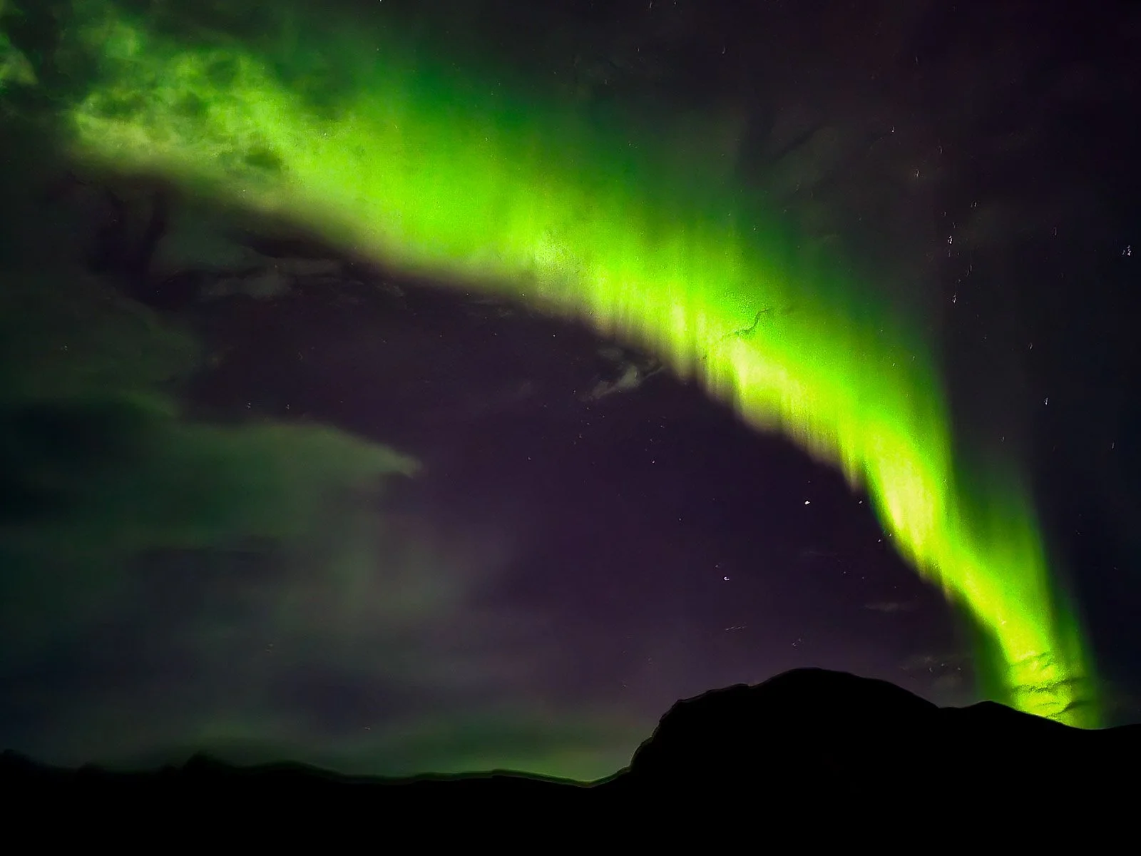 Bright green Northern Lights sweeping across the night sky above dark mountains in Iceland
