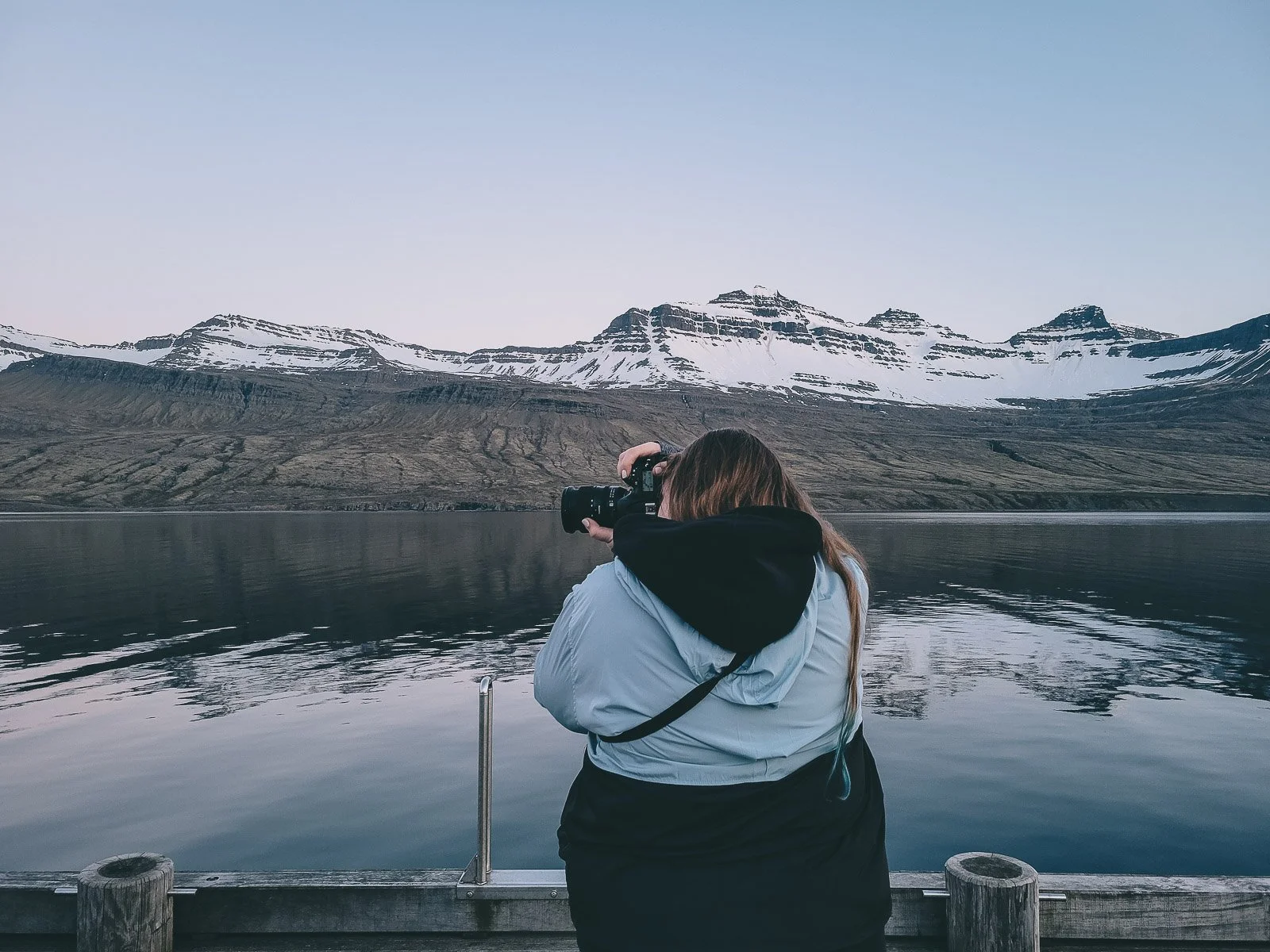 Photographer taking a photo of snow-covered mountains across the water in Iceland