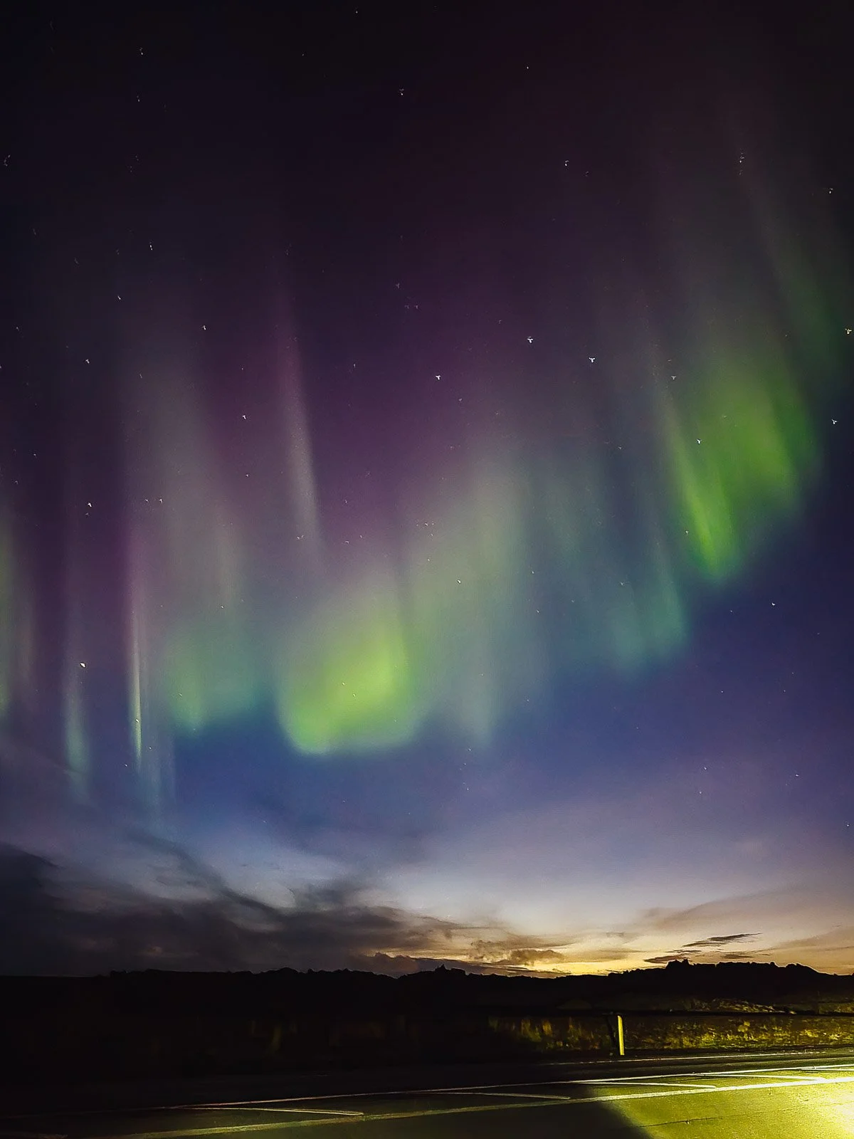 Green and purple Northern Lights above a road and dark landscape in Iceland