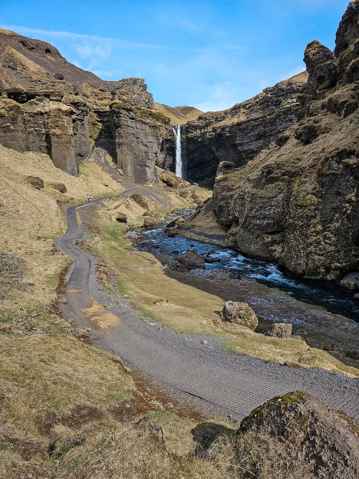 Trail leading through a rocky canyon toward Kvernufoss waterfall in Iceland, with a river flowing beside the path.
