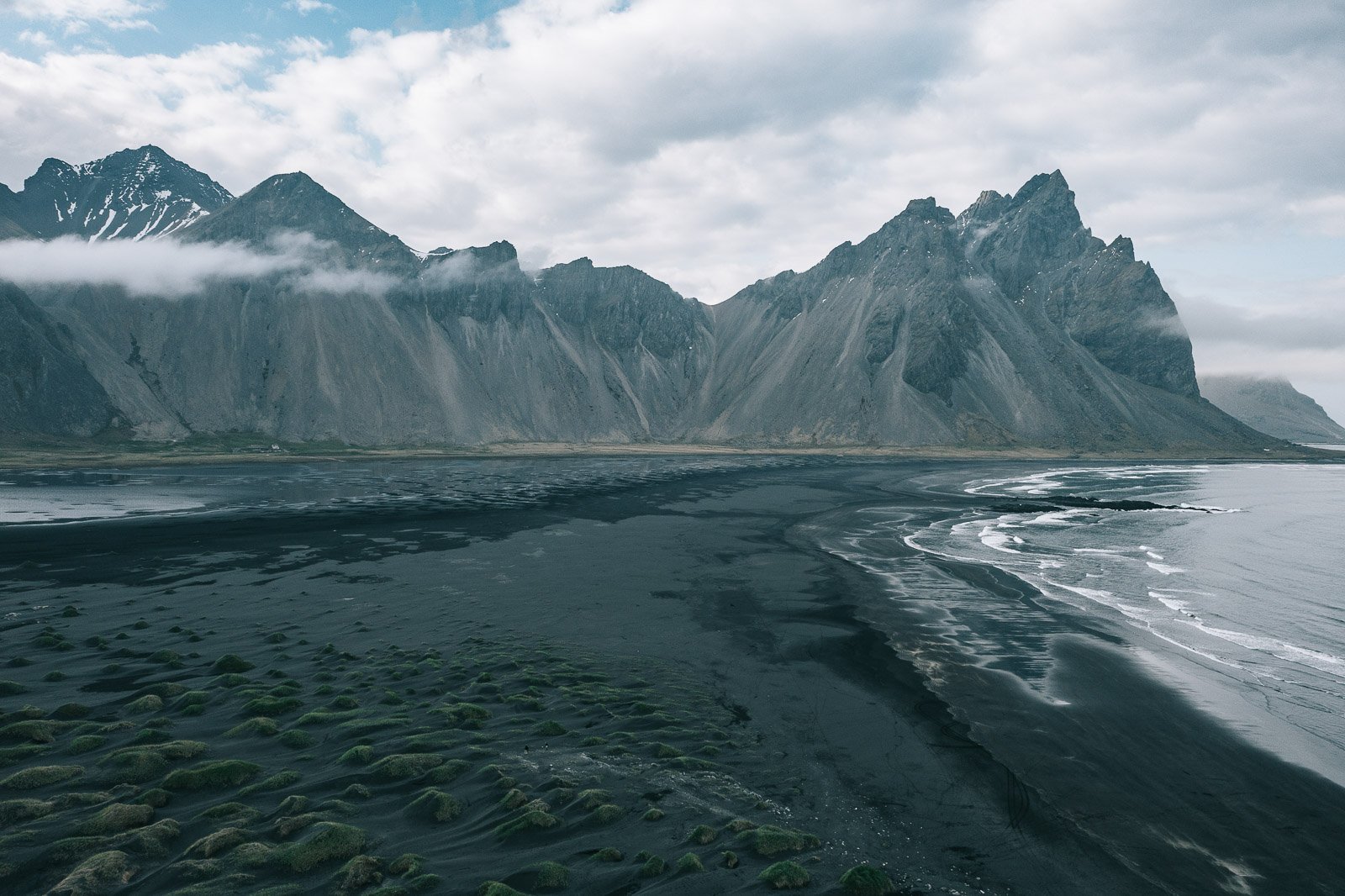Vestrahorn mountain behind the black sand beach at Stokksnes in Iceland, with low clouds along the mountain peaks.