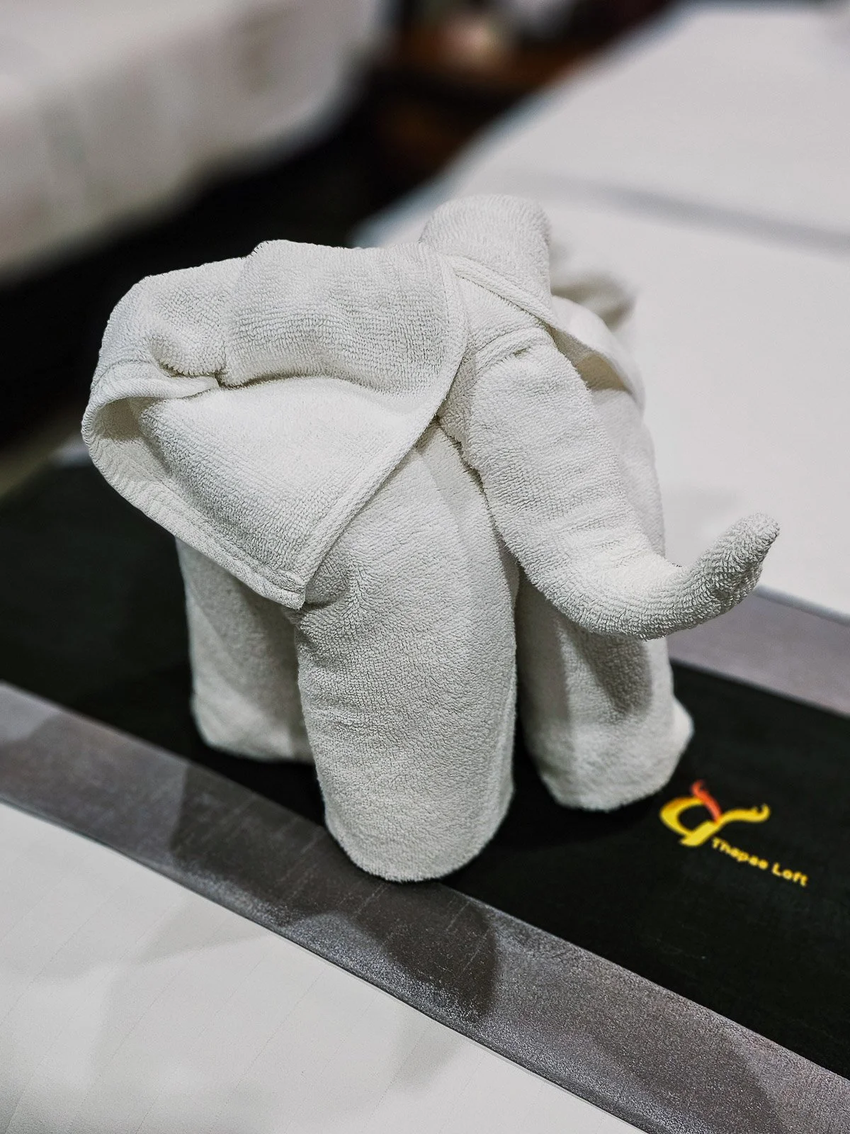 Elephant folded from white towels and placed on a bed.
