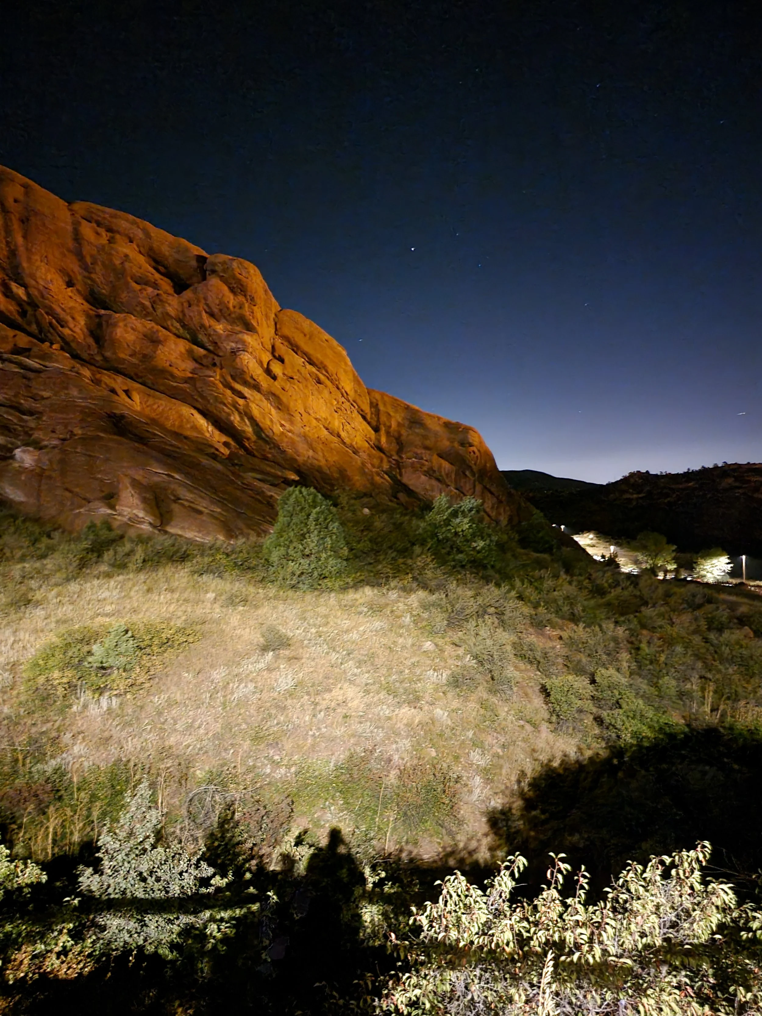 large orange rock formation at night with a grassy field in front and a night time sky with stars
