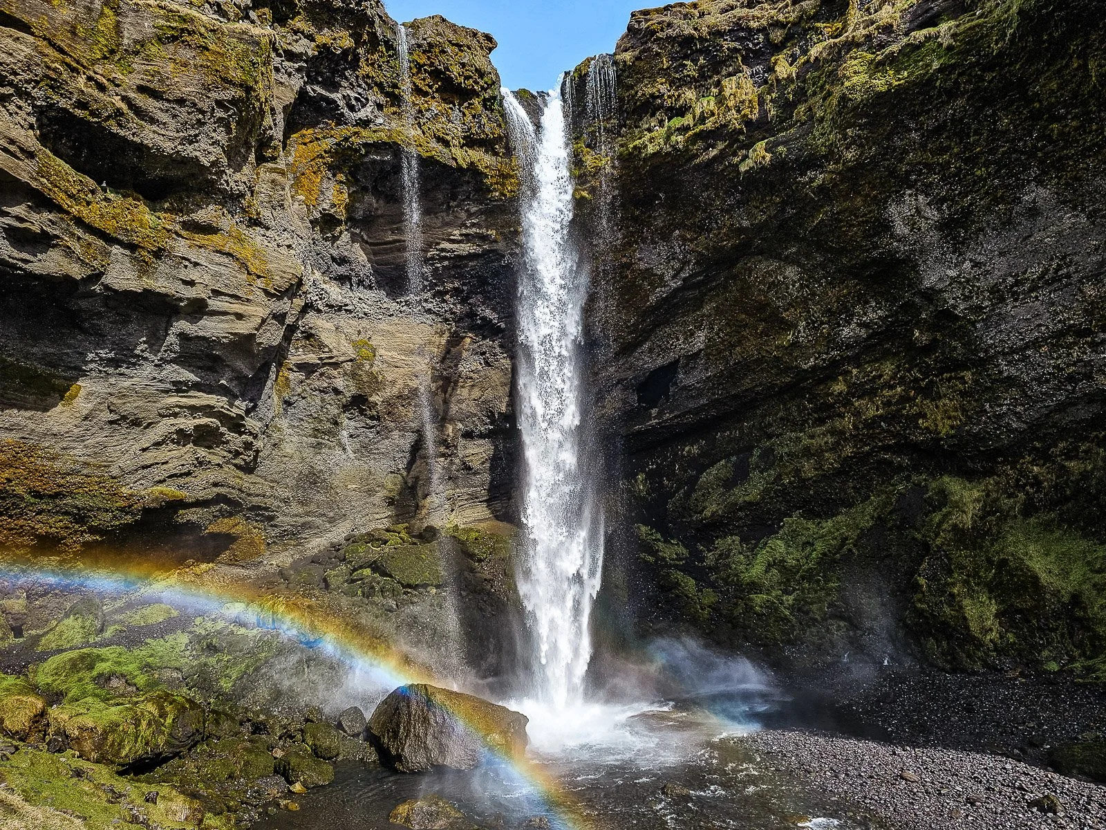 Kvernufoss waterfall flowing into a rocky gorge with a rainbow in the mist