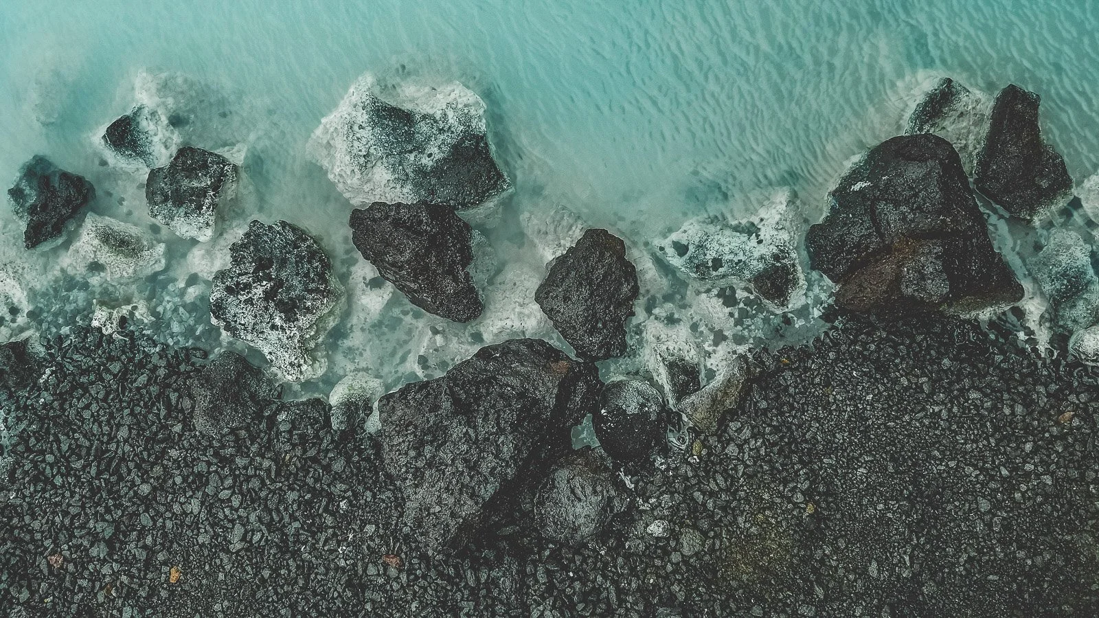 Milky blue geothermal water surrounding black lava rocks at the Blue Lagoon in Iceland