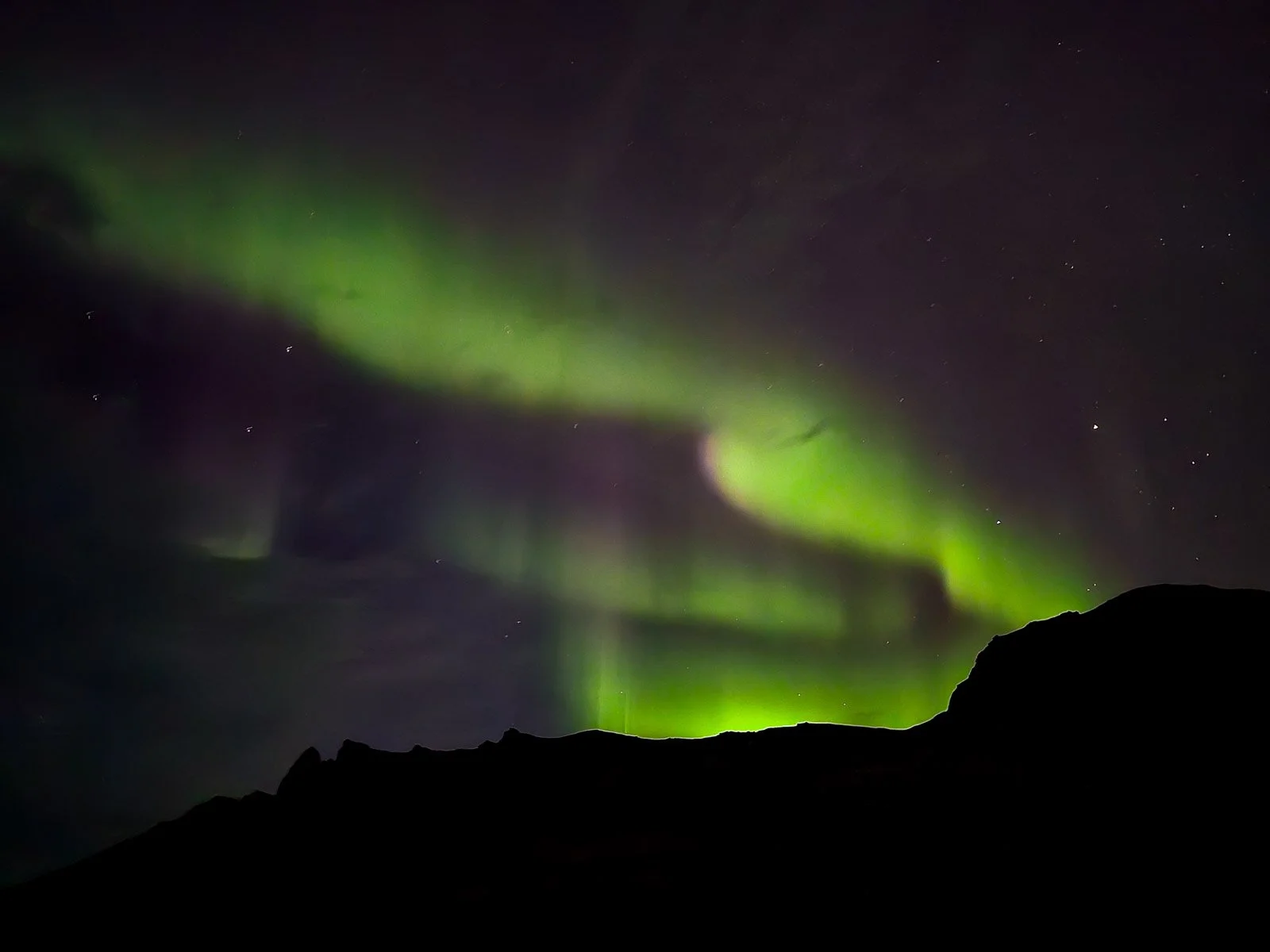 Green Northern Lights stretching across the night sky above dark mountains in Iceland