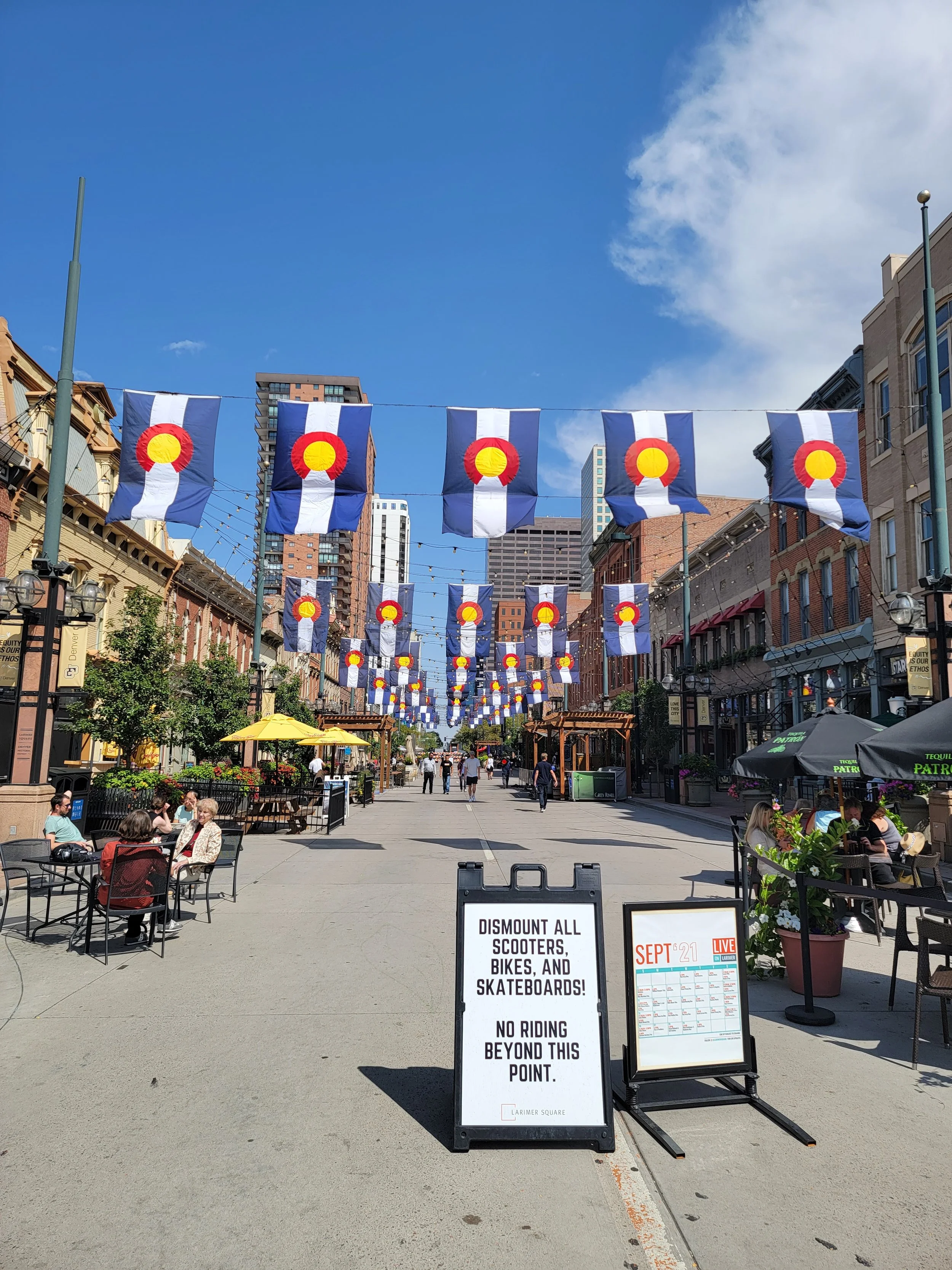 walking street in denver colorado with a large brick building and colorado flags hanging from wires across the street on multiple strings