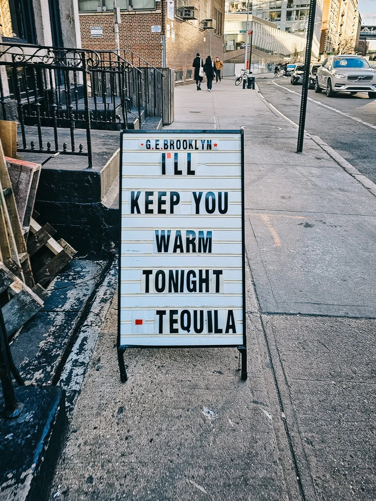 Sidewalk sign outside G.E. Brooklyn reading “I’ll keep you warm tonight – tequila” on a Brooklyn street.