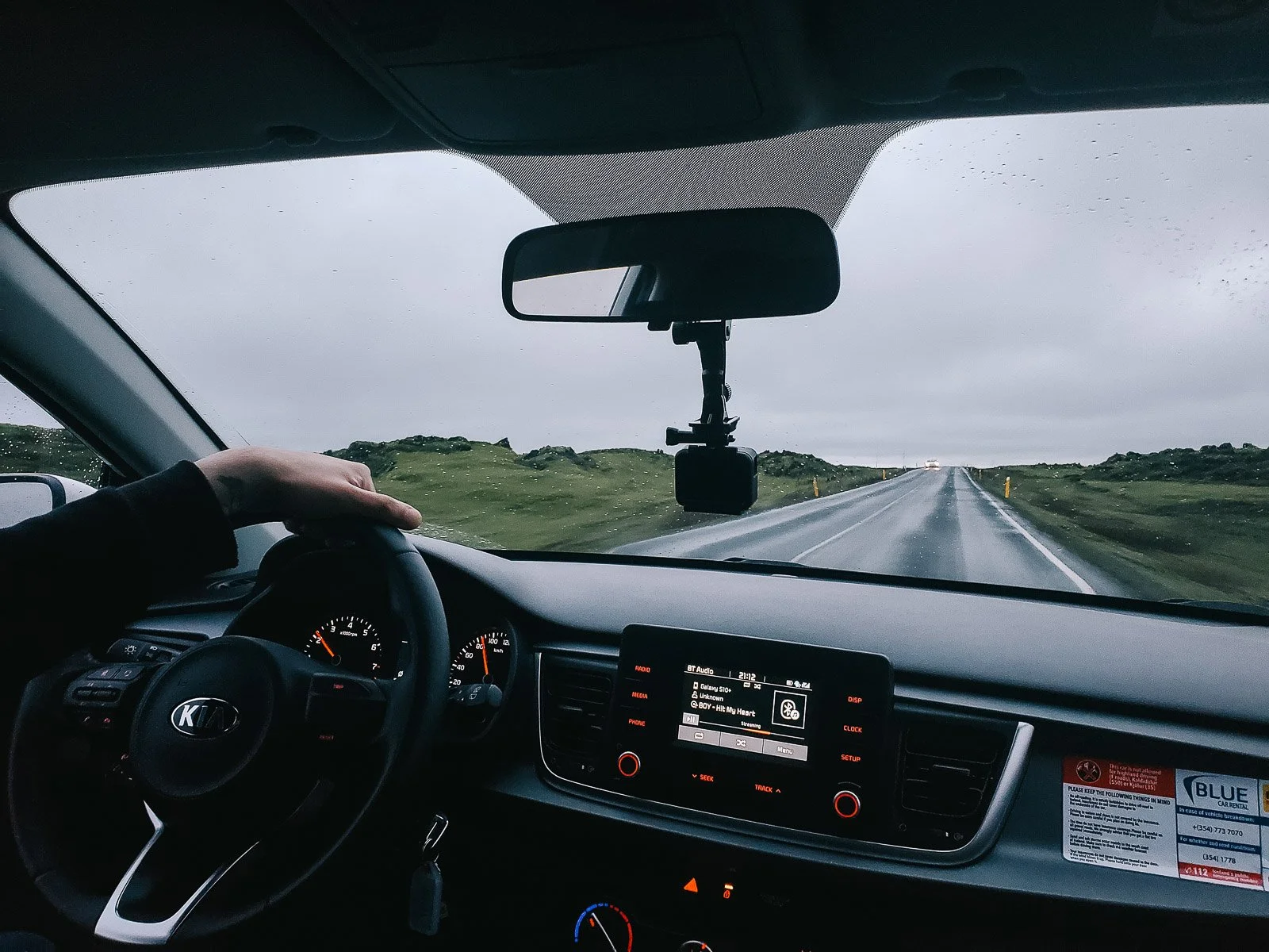 View from inside a rental car driving on a wet road through the Icelandic countryside