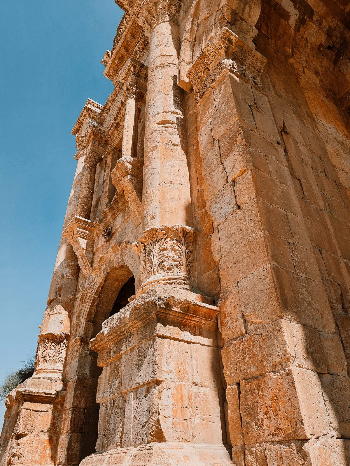 Detailed stone columns and carved Corinthian capitals on Hadrian’s Arch in Jerash, Jordan, against a blue sky.