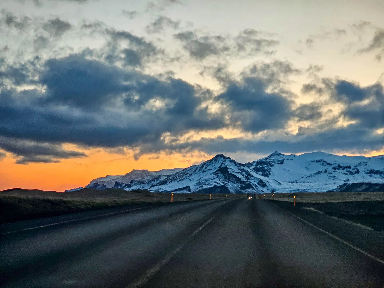 Road through Iceland leading toward snow-covered mountains at sunset