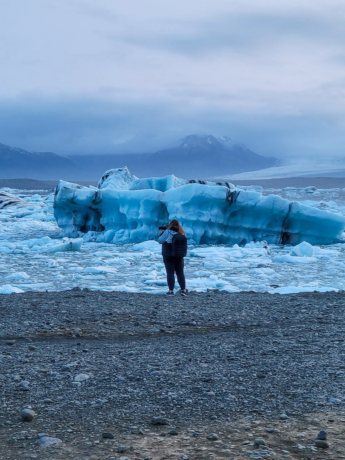 Photographer taking a photo of blue icebergs at a glacial lagoon in Iceland