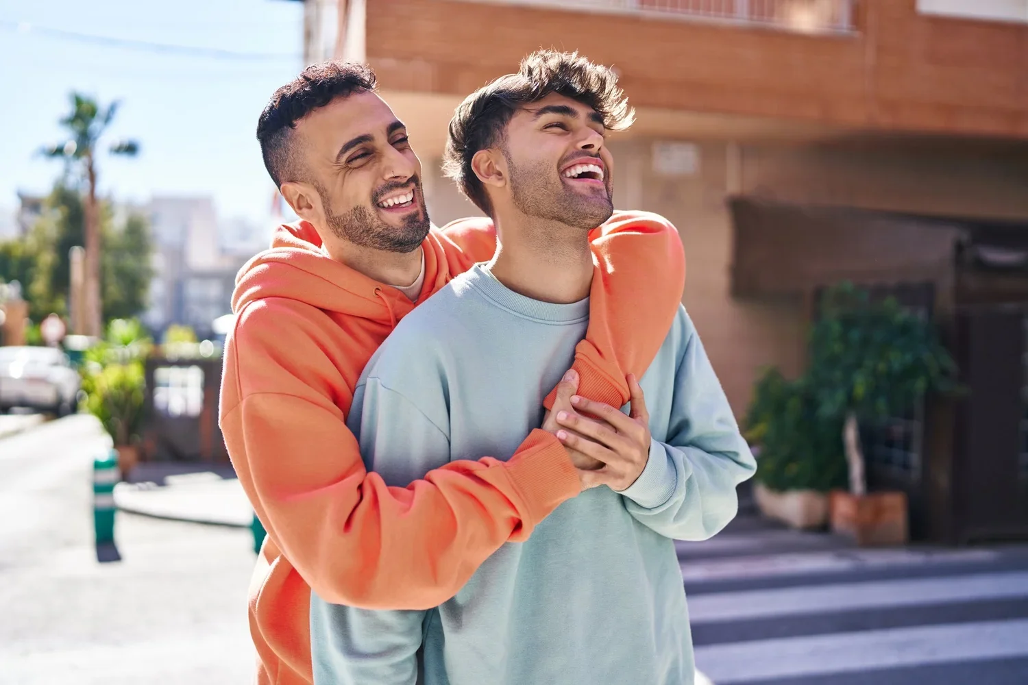 A happy male couple embracing and laughing outdoors on a city street