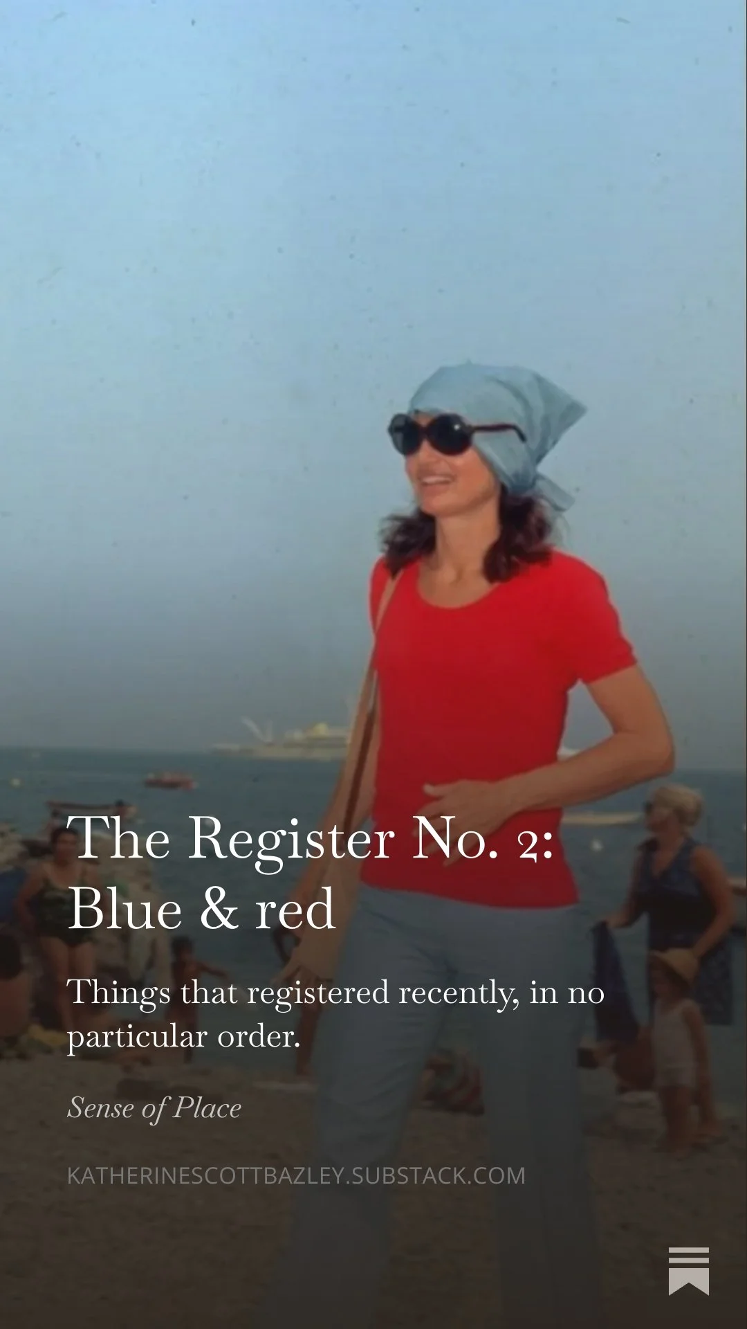 Jackie O on Capri in a red shirt, blue headscarf, and sunglasses smiling at the beach. There are other people in the background near the water.