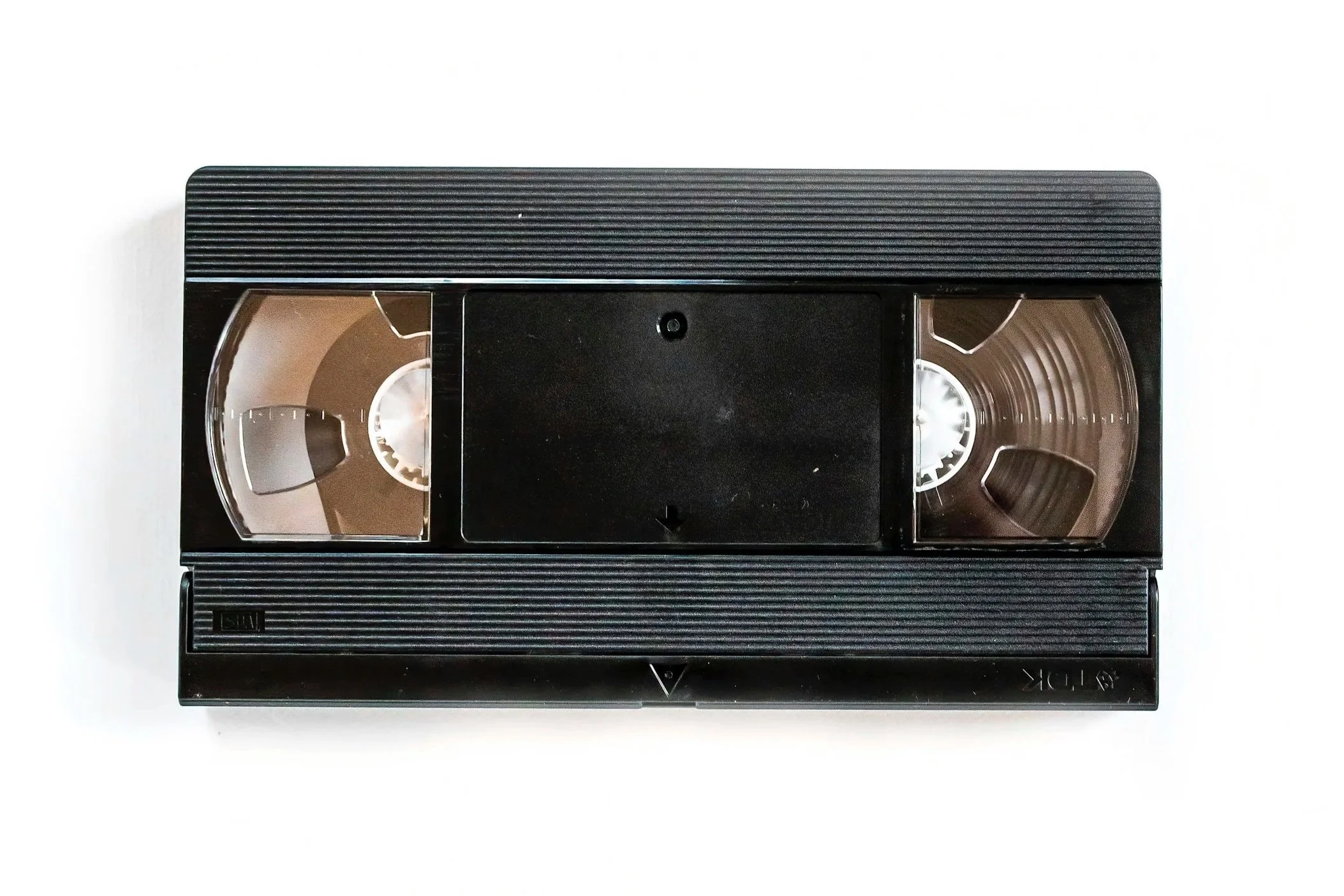 A black VHS tape with transparent reels, viewed from above, on a white background.