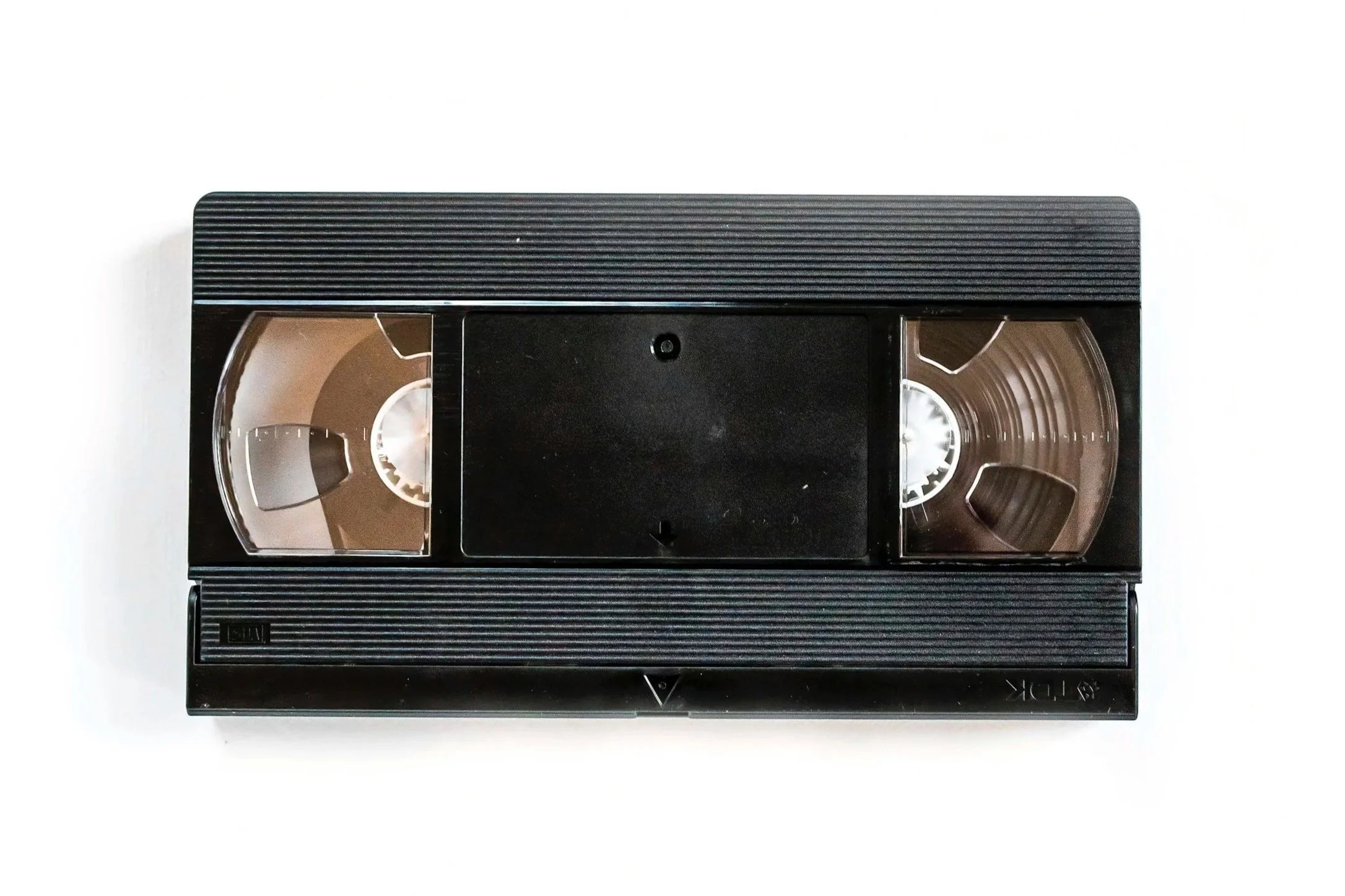 Top view of a black VHS tape with clear windows showing spools of tape inside, placed on a white surface.