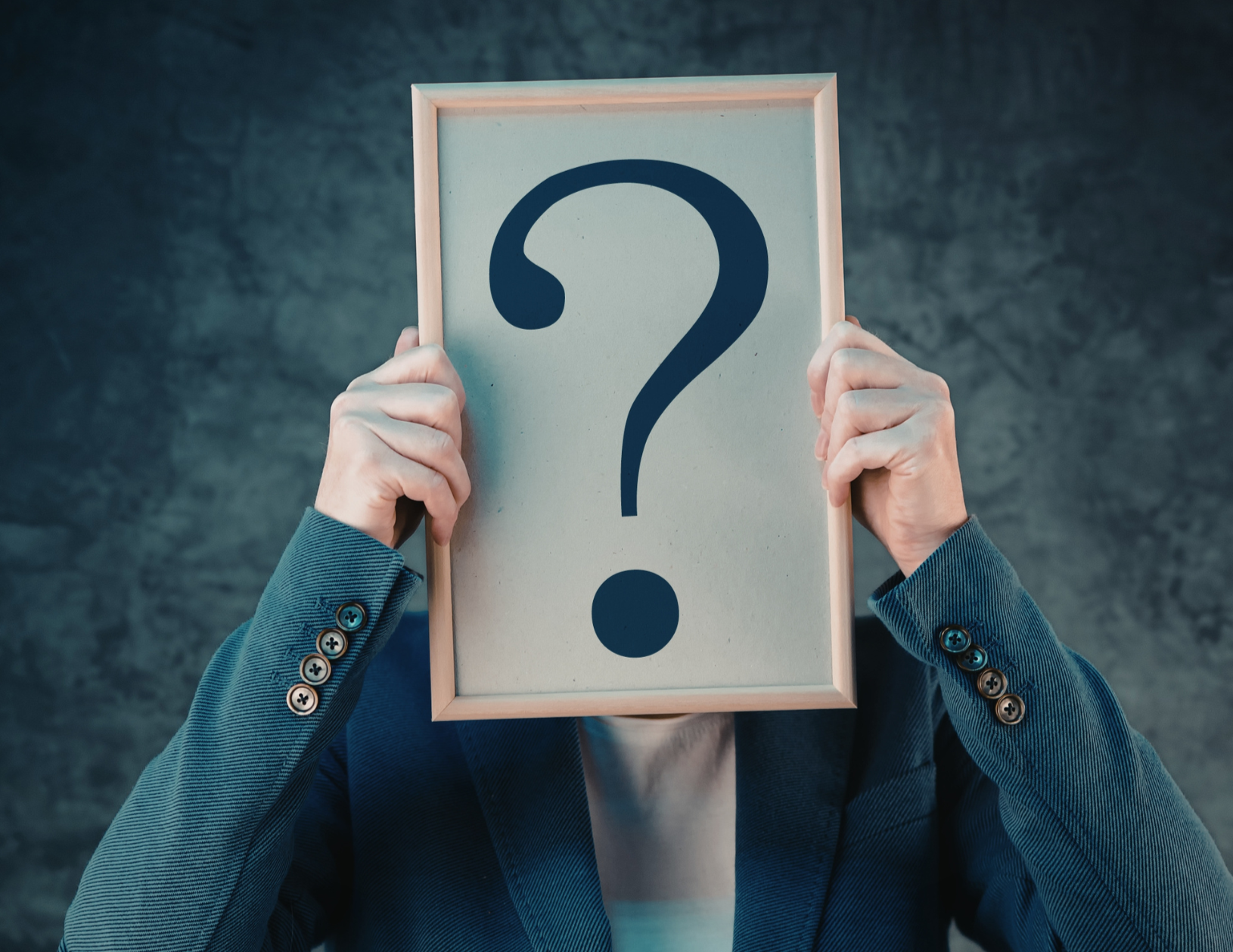 Person in a suit holding a frame with a large question mark in front of their face.