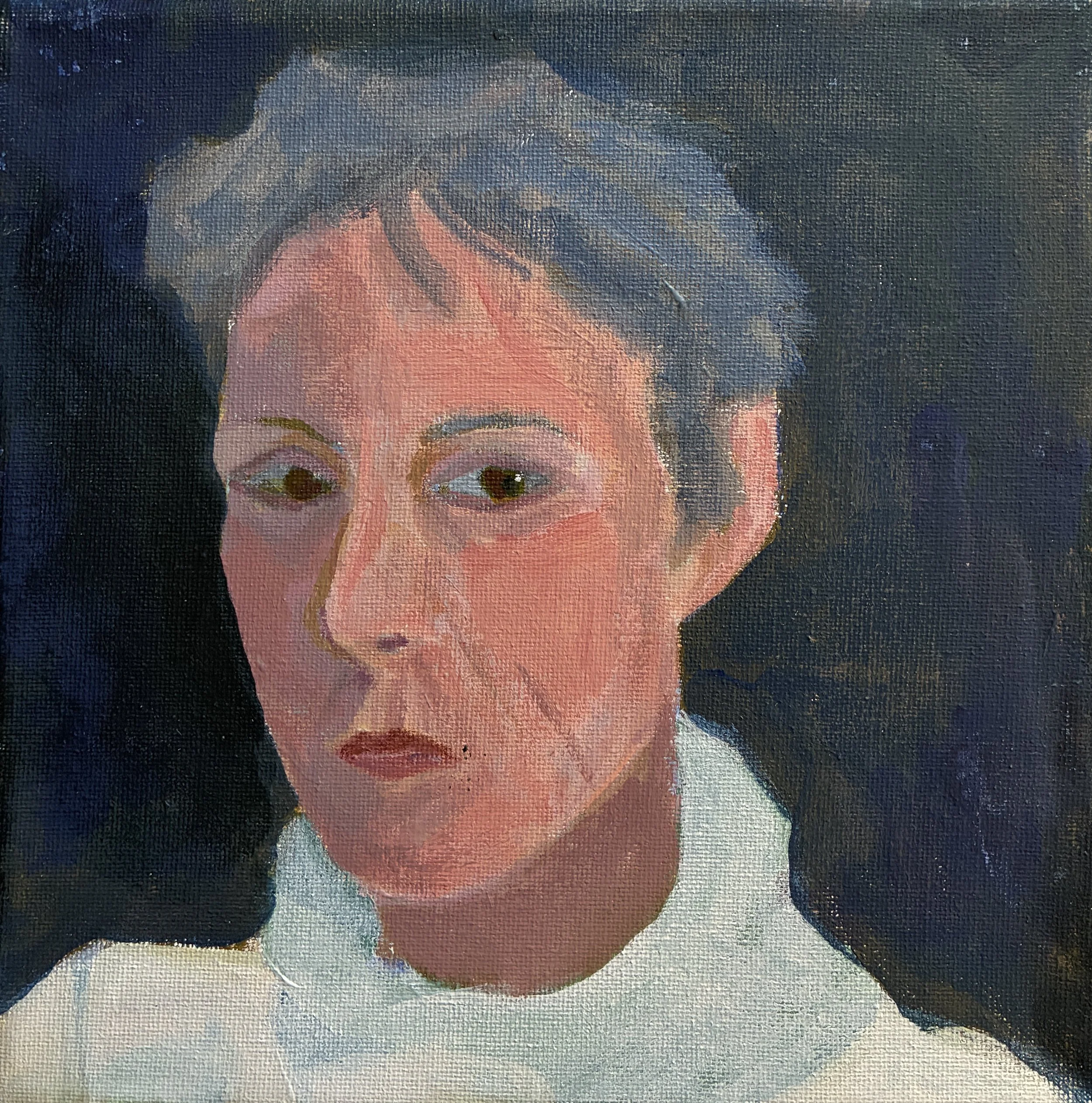 An older woman with short gray hair sitting on a wooden dock by a stream in a wooded area.