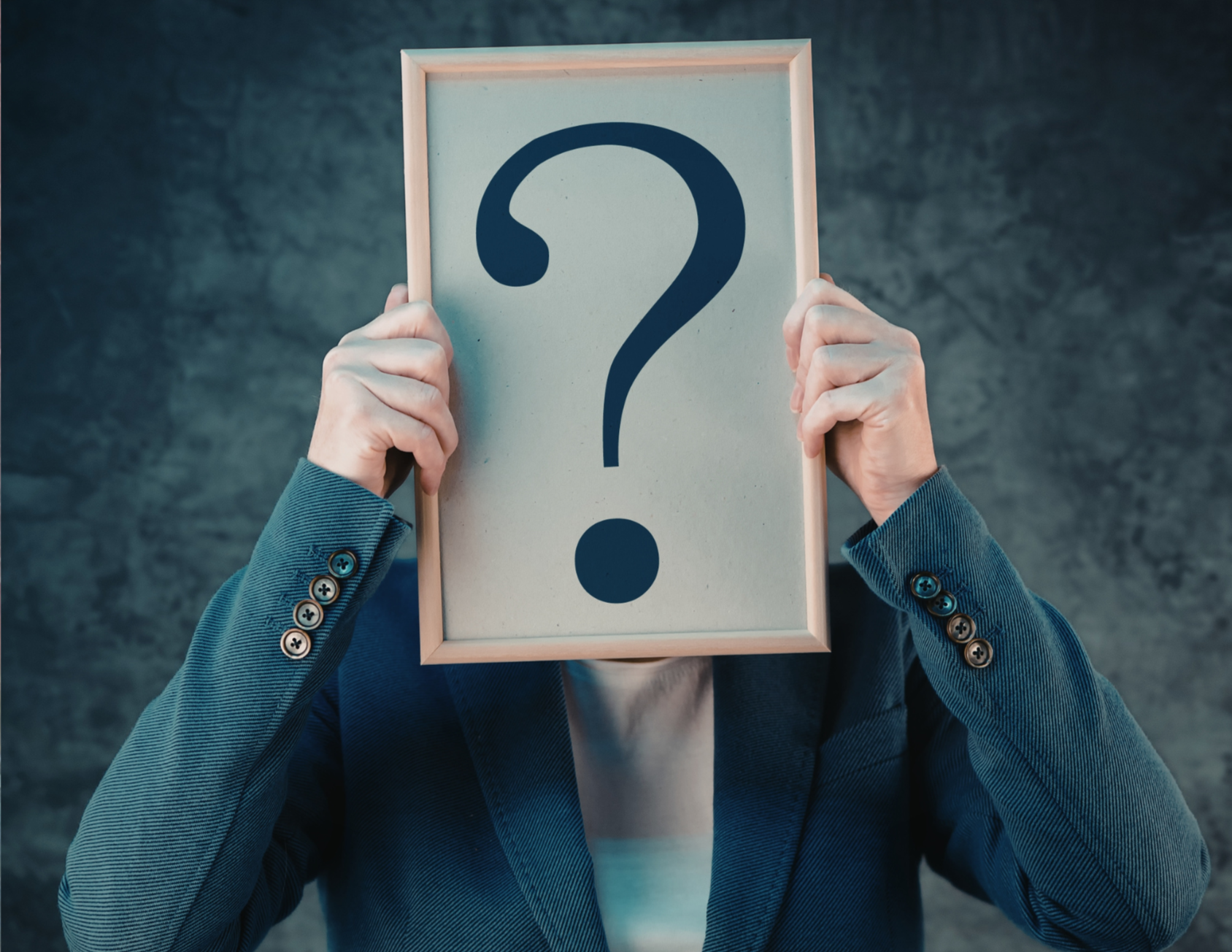 Person in a business suit holding a frame with a large question mark in front of their face.