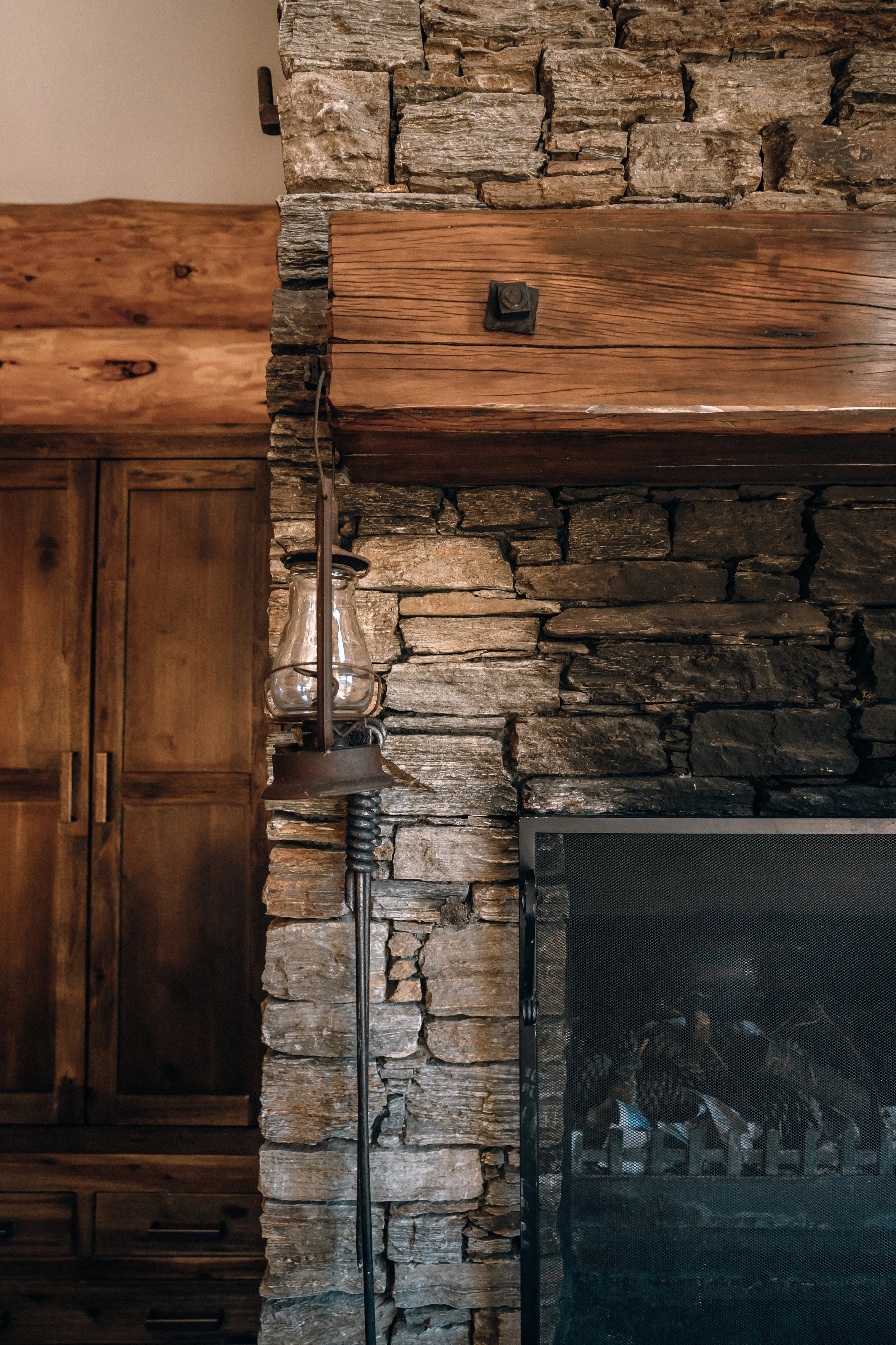 A rustic interior with a stone and wood fireplace, a wooden cabinet, a vintage lamp, and a tapestry on the wall.