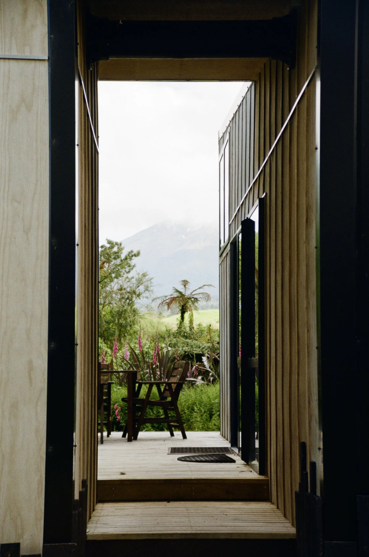 View through an open doorway showing a garden with chairs, plants, trees, and a mountain in the background.