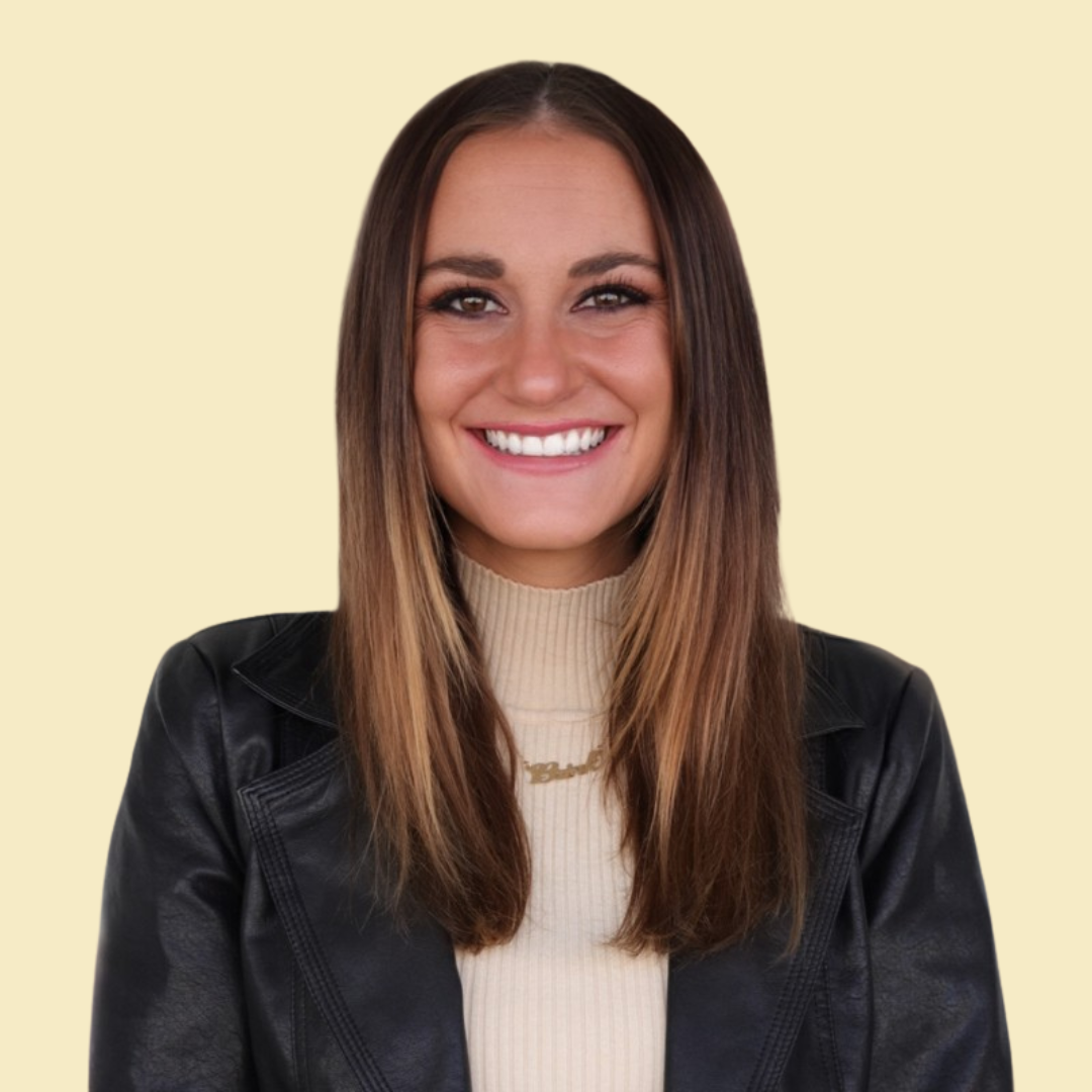 A girl with dark hair that fades to blonde hair with her hair down wearing a black top against a light yellow background
