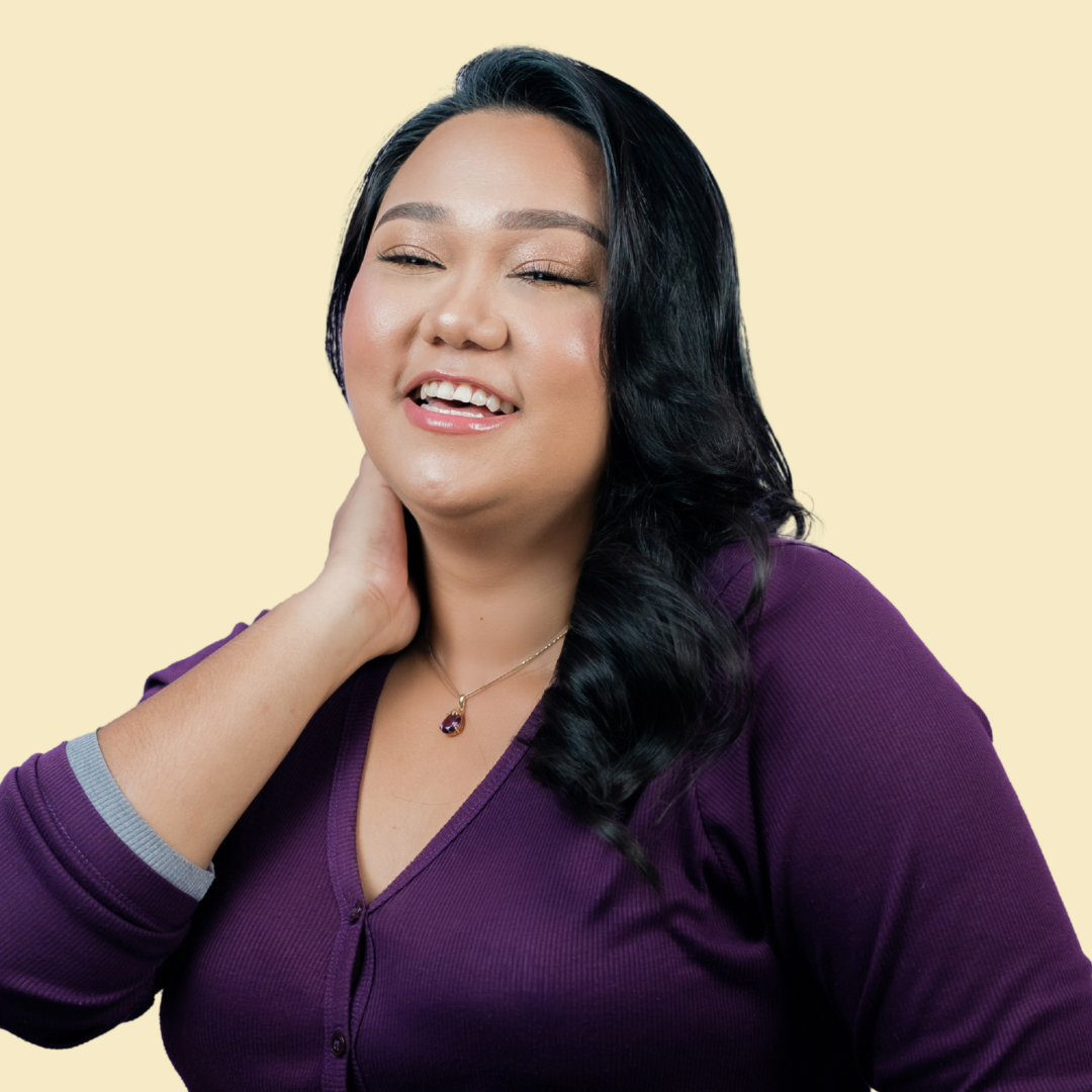 A smiling woman with long black hair, wearing a purple top and a necklace, against a solid light yellow background.